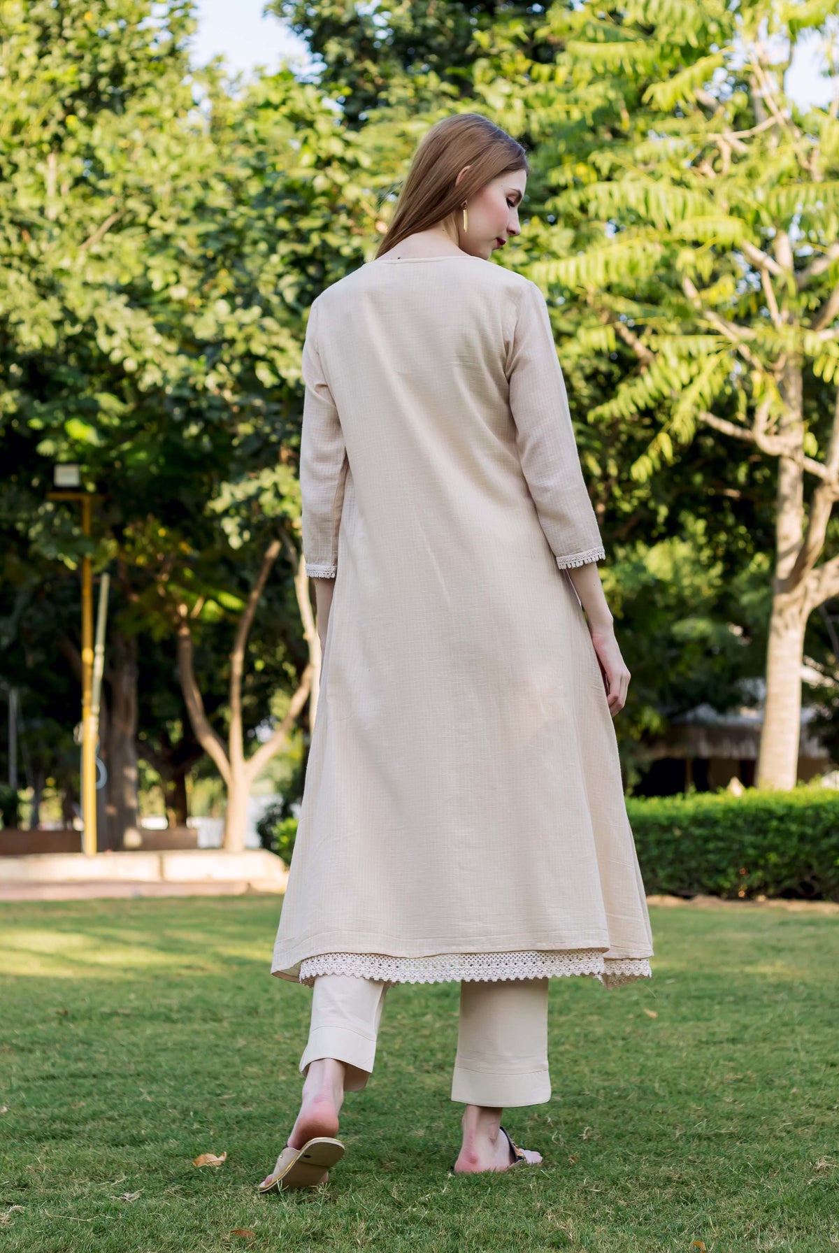 Beige embroidered kurta with delicate lace trim and pants worn by a model from back.