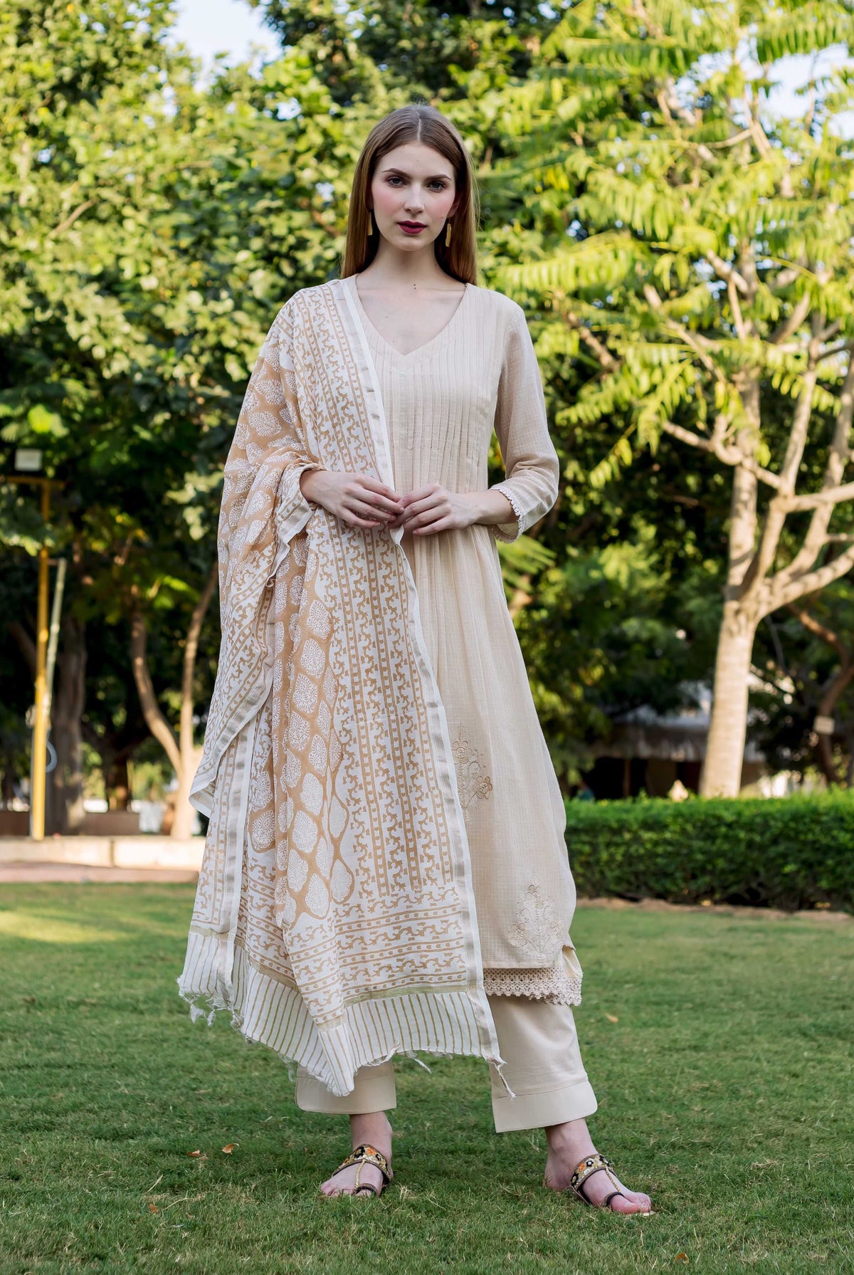 Model in beige embroidered kurta set with block-printed dupatta, standing on a lawn.