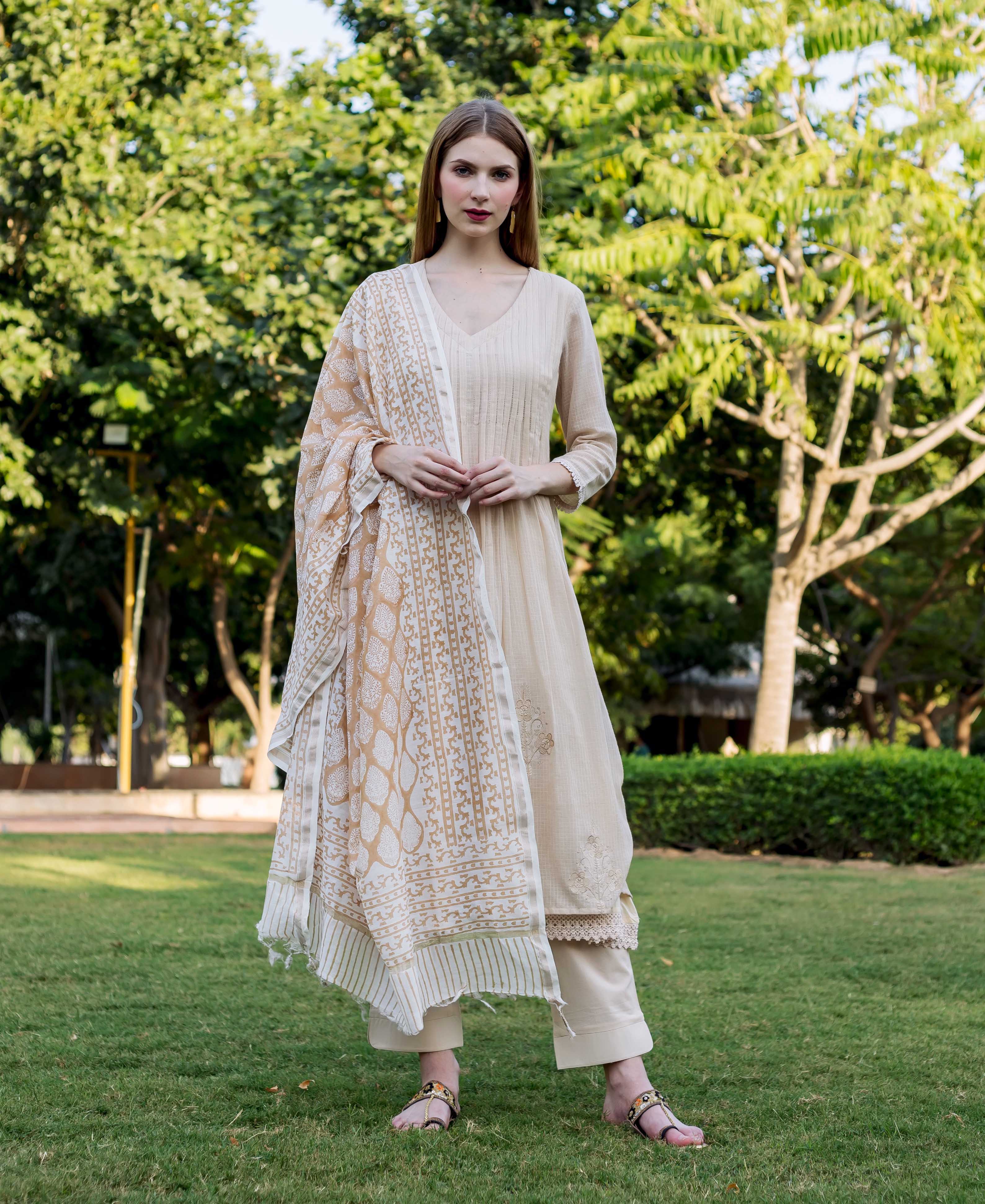 Model in beige embroidered kurta set with block-printed dupatta, standing on a lawn.