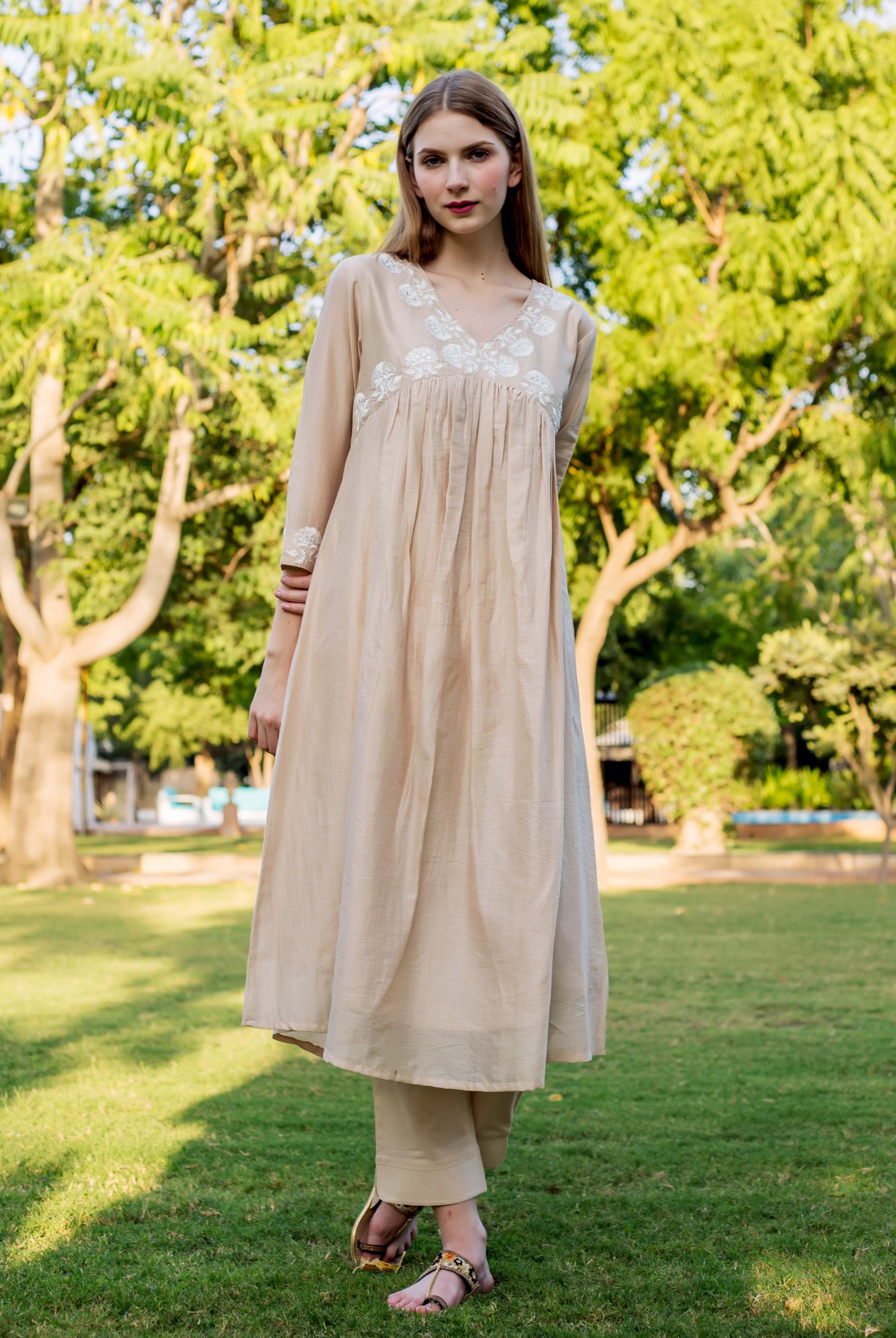 Front view of a model wearing a beige kurta with white embroidery and matching trousers.