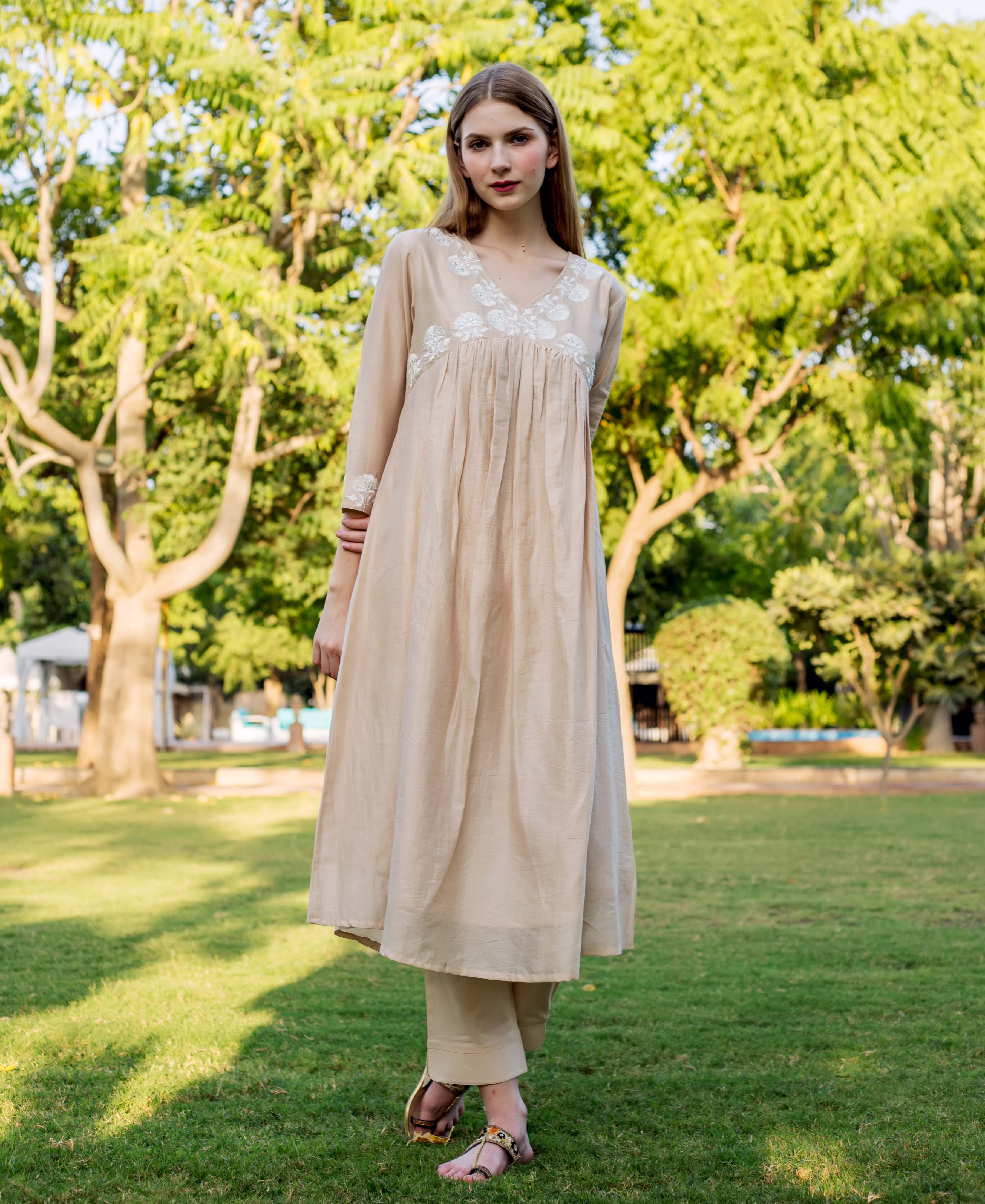 Front view of a model wearing a beige kurta with white embroidery and matching trousers.