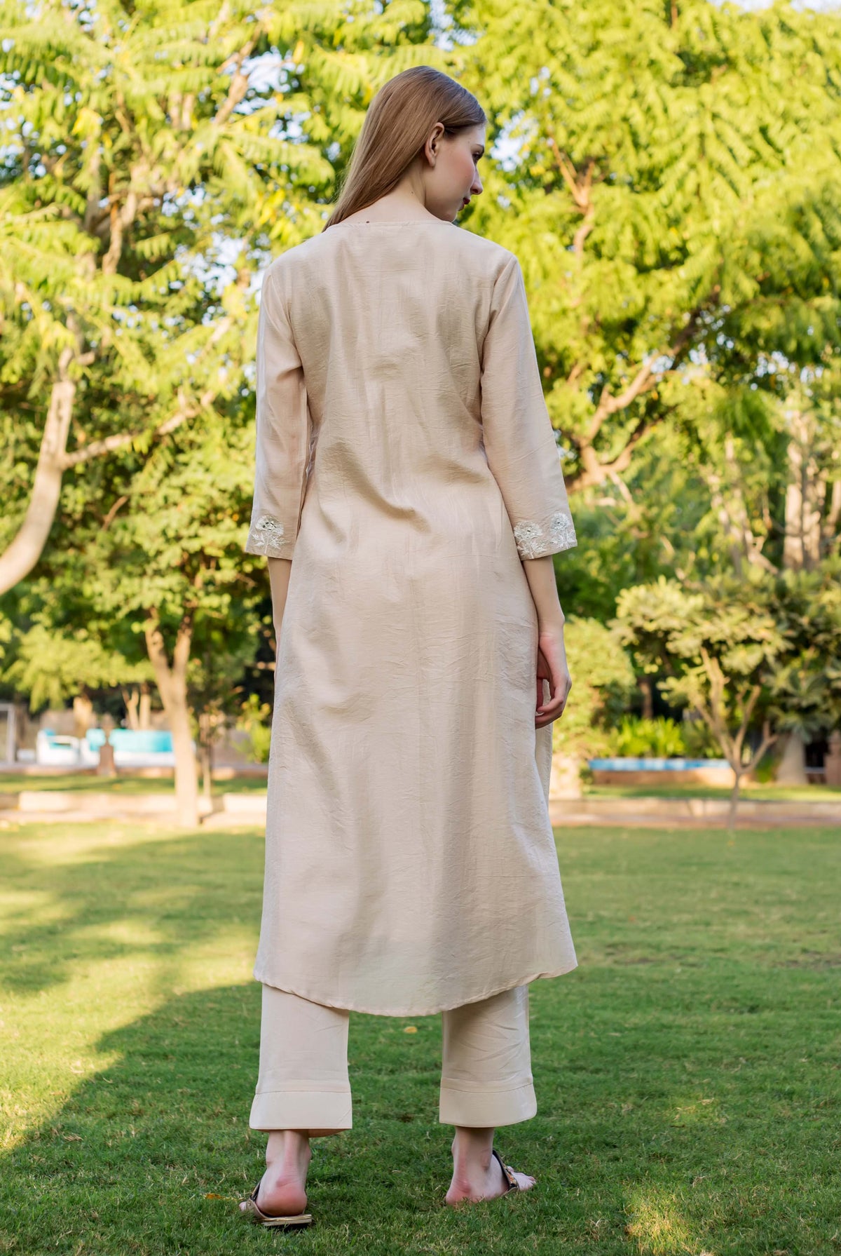 Beige chanderi embroidered kurta and pants on model standing in outdoor setting.