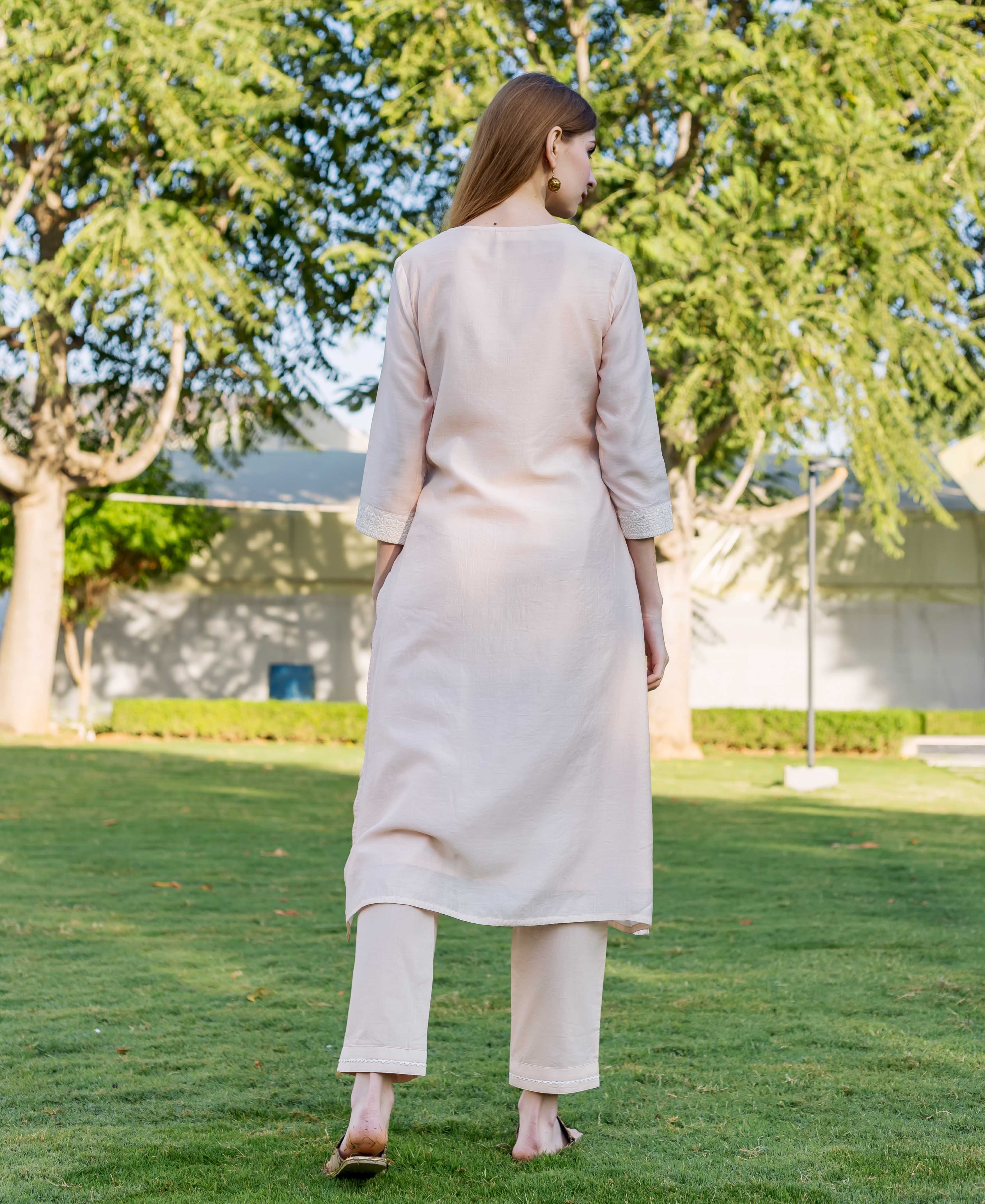 Back view of model wearing baby pink kurta set with white lace trim.