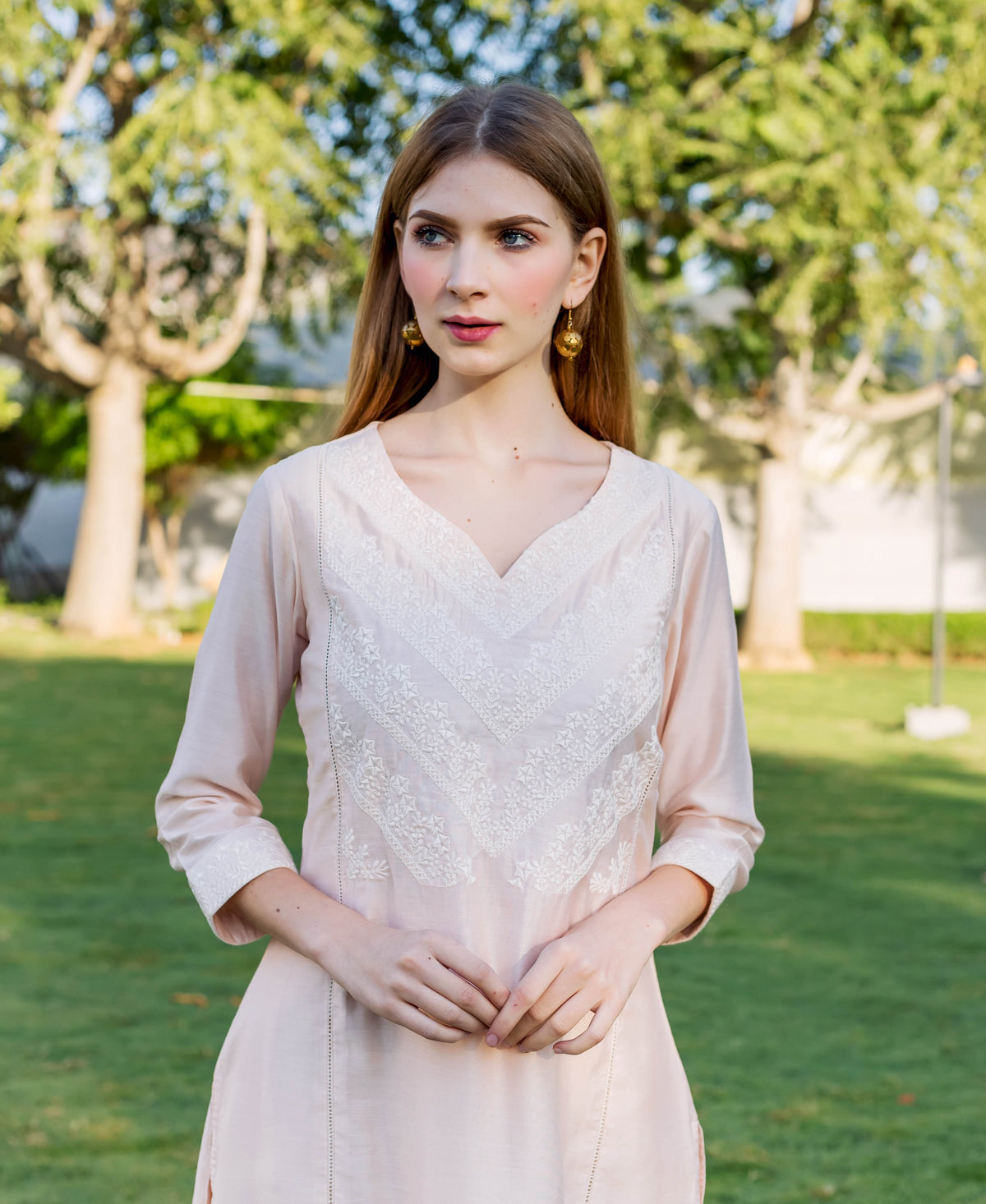 Model wears a baby pink kurta with white V-shaped embroidery, standing outdoors.