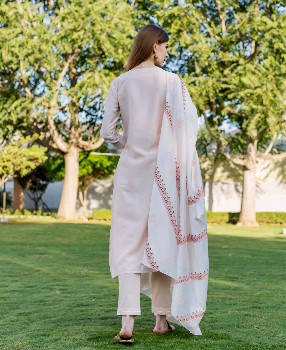 Rear view of model in a baby pink kurta set with a white hand-block-printed dupatta.