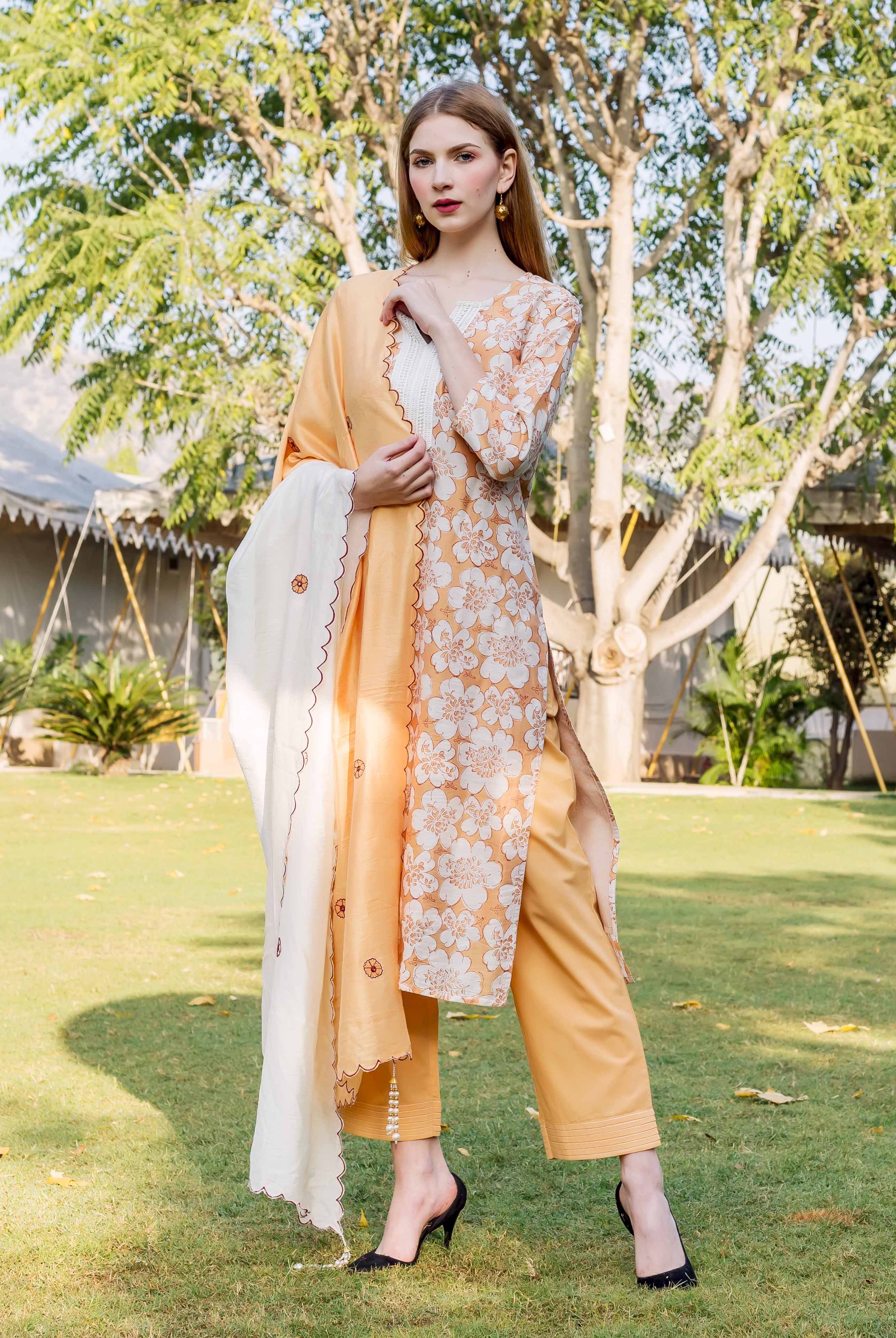 Front view of model in golden yellow floral block printed kurta set with white dupatta.