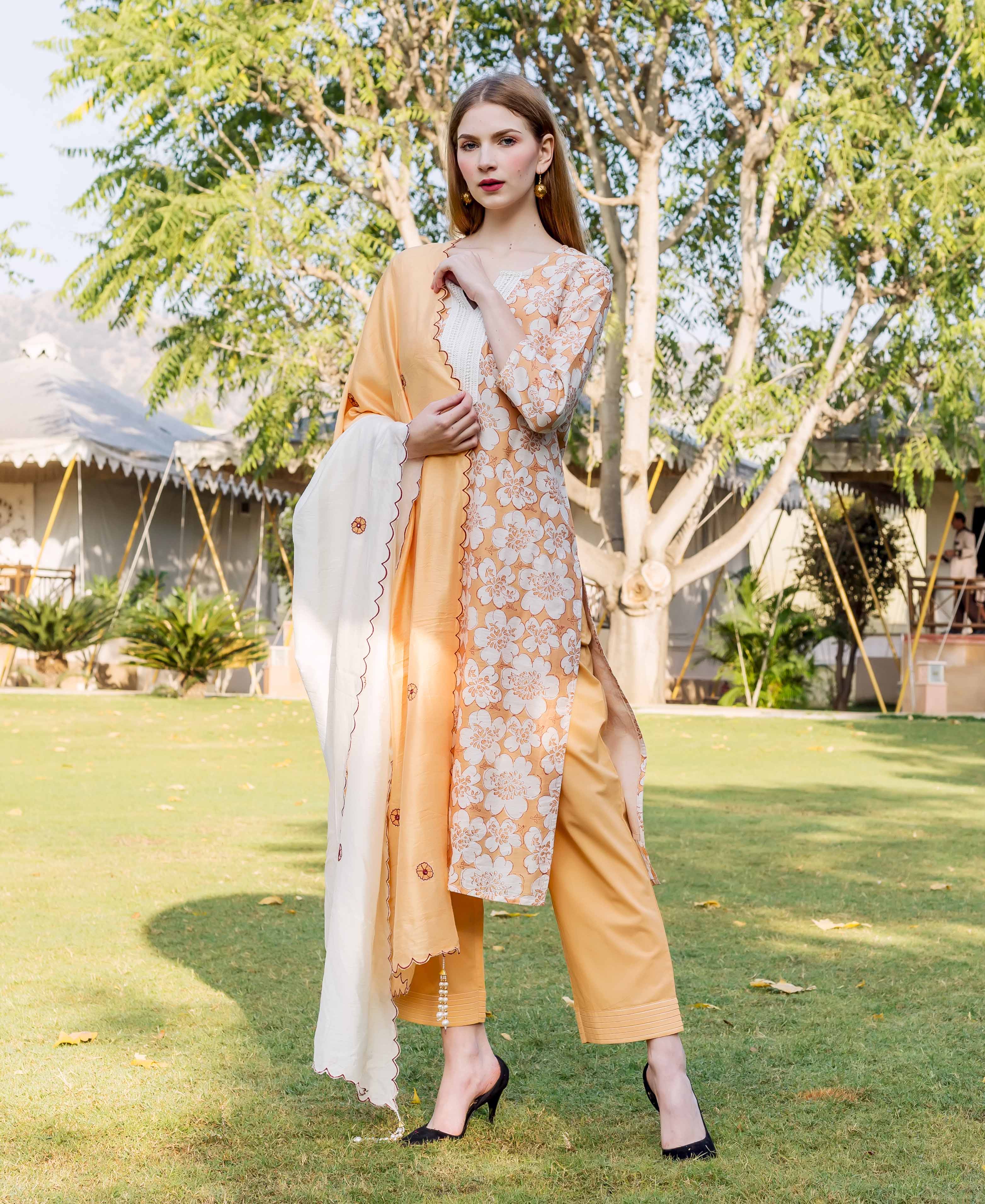 Front view of model in golden yellow floral block printed kurta set with white dupatta.