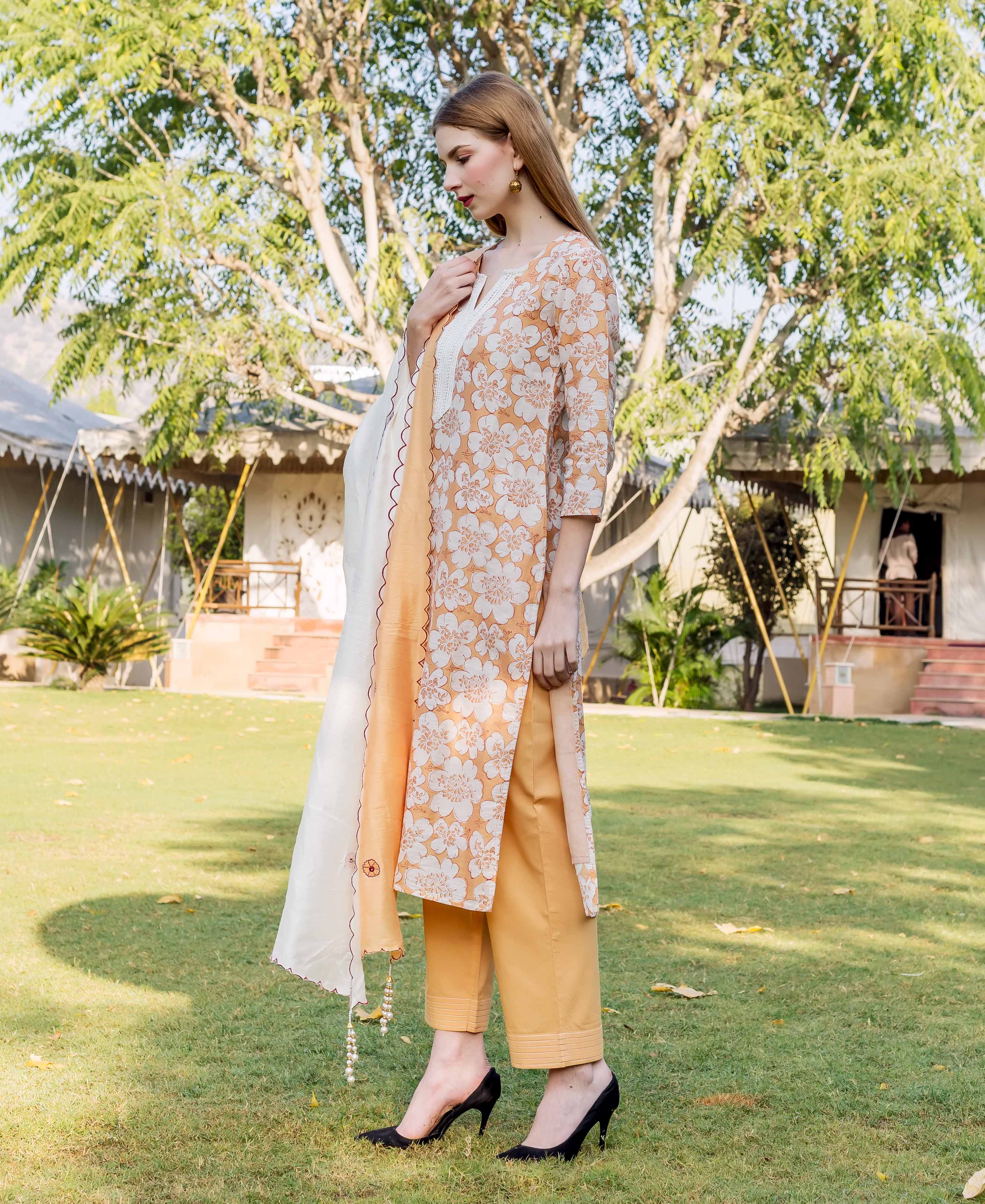 Orange and white floral patterned long tunic, mustard pants, and white scarf on a model outdoors.