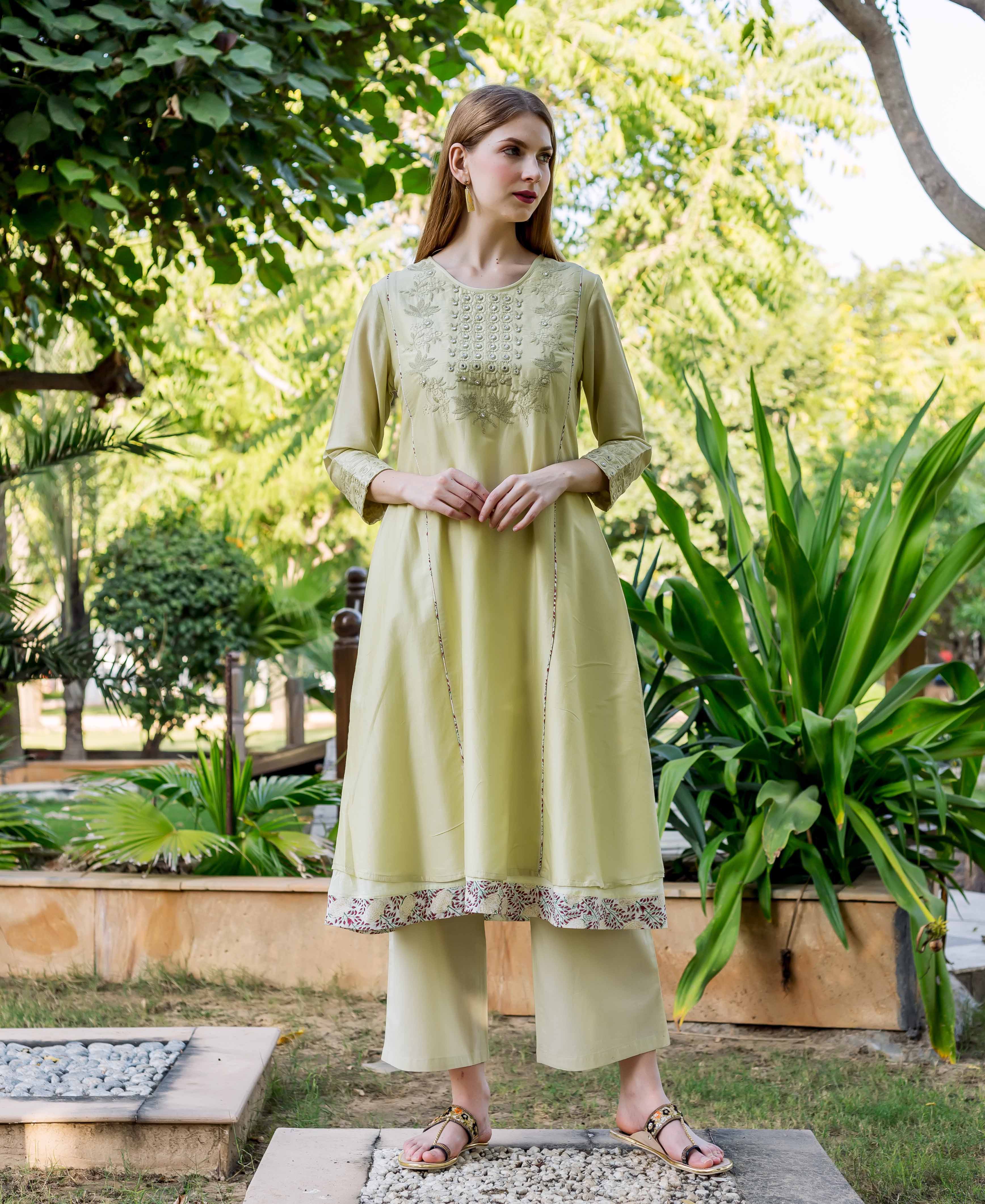 Model wearing light green embroidered A-line kurta with floral printed hem and pants.