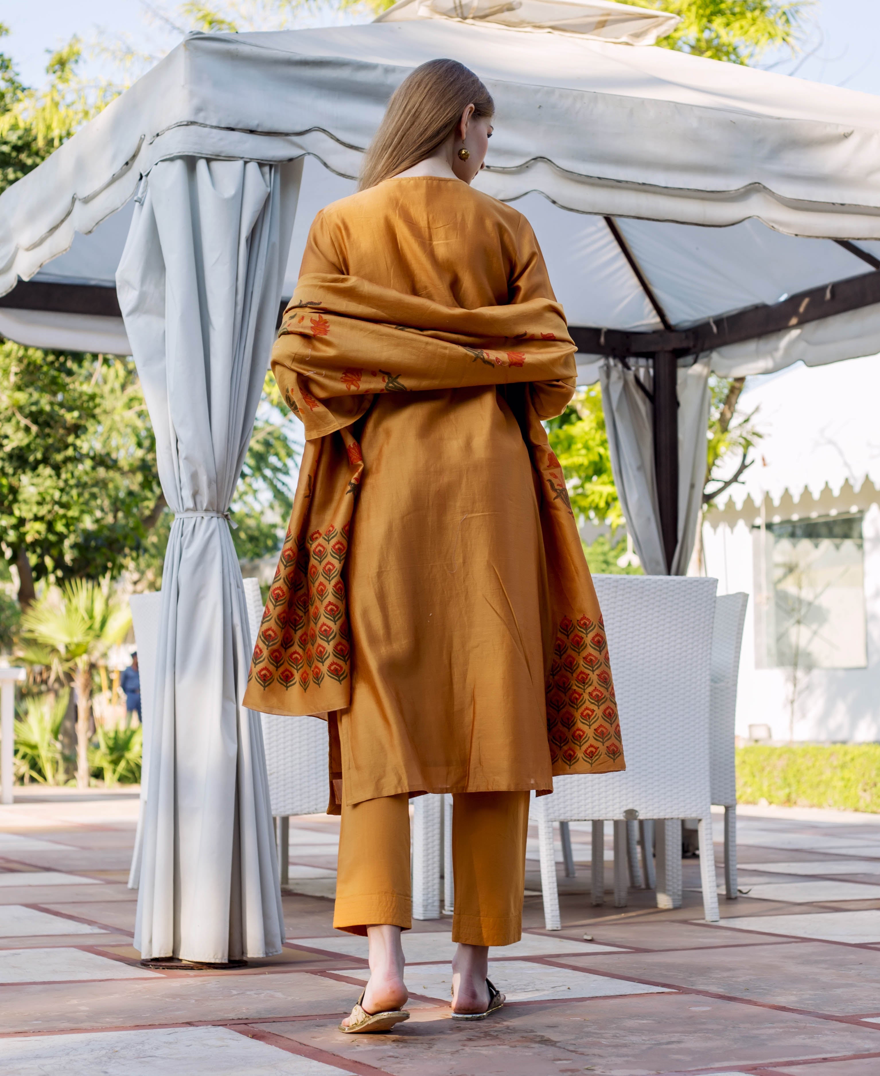 Back view of model in an autumn rust hand-block-printed kurta, pants, and matching dupatta.
