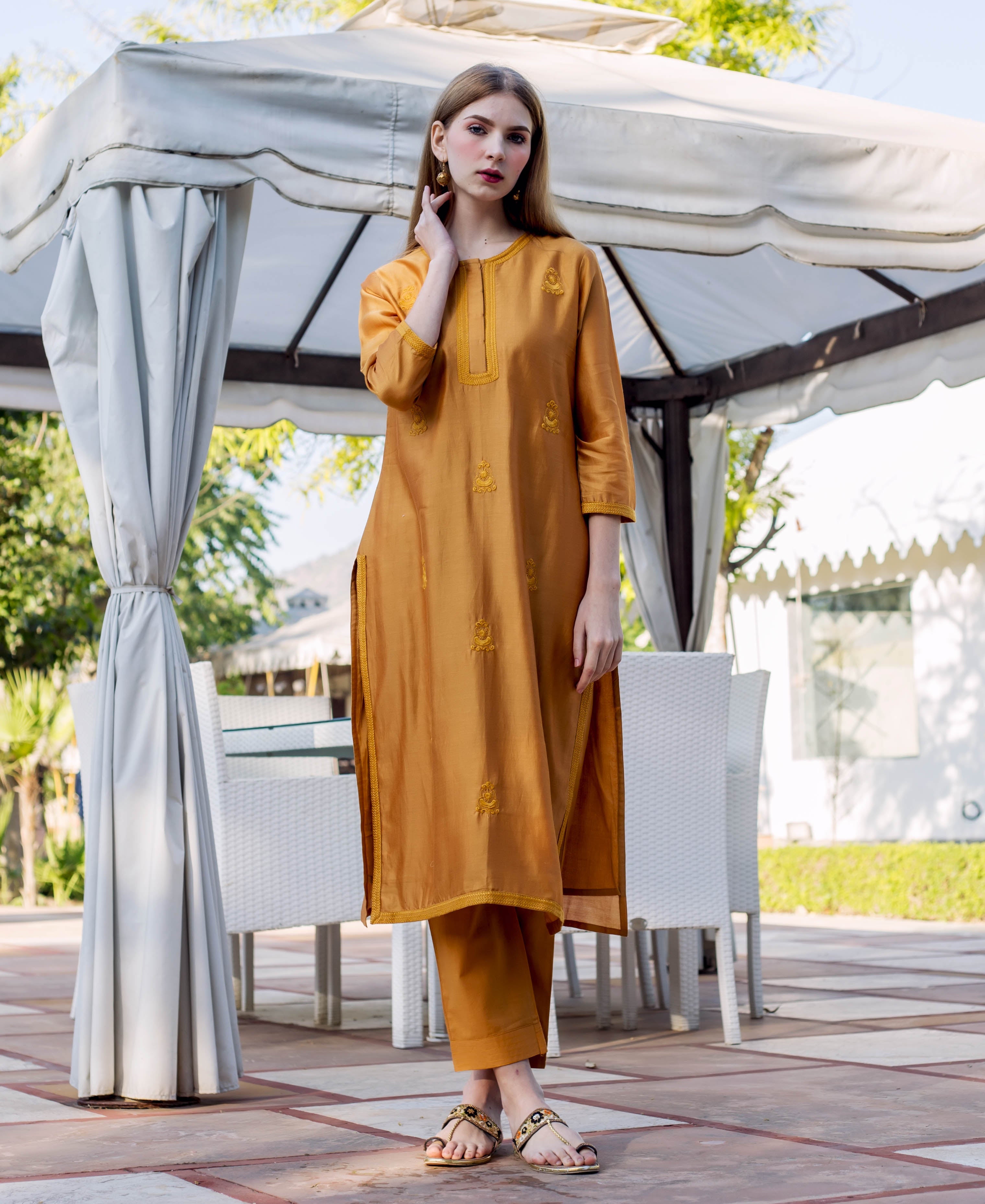 Model in autumn rust kurta and pants with gold embroidered motifs, front view.