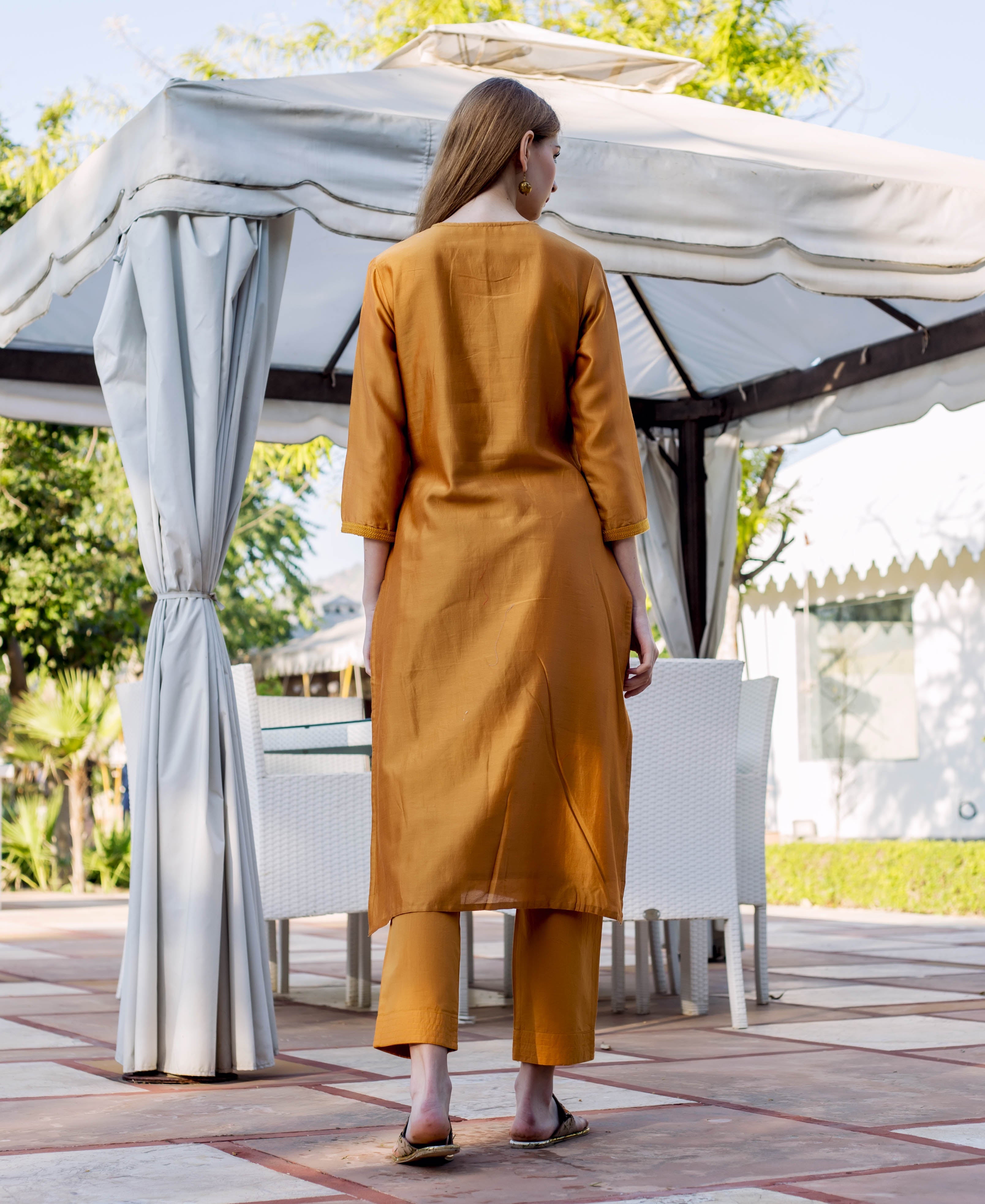 Back view of model in an autumn rust kurta and pants with subtle sleeve trim.