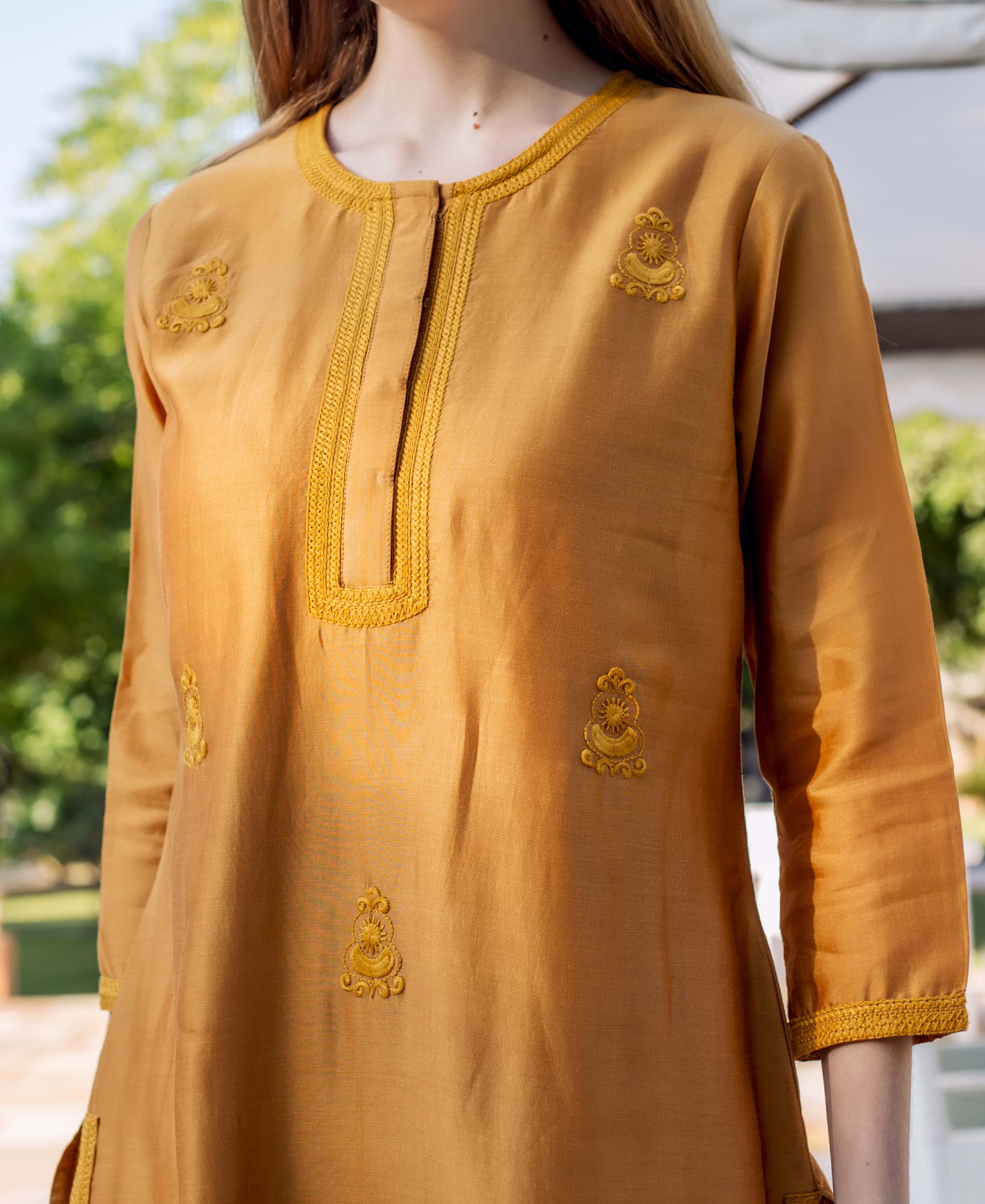 Woman wearing mustard-yellow embroidered kurta with intricate yellow designs and trim.