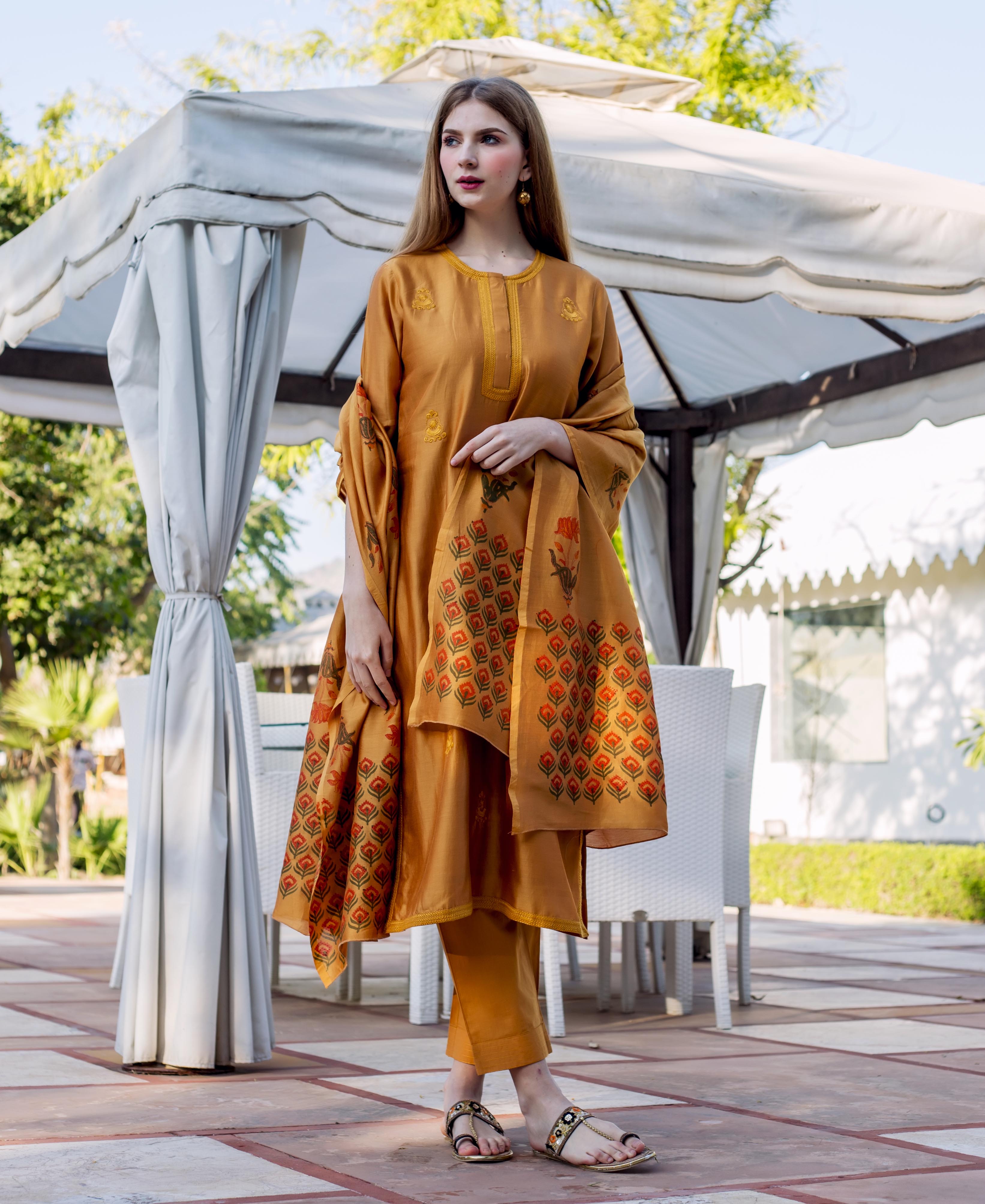 Model wears an autumn rust embroidered kurta set with detailed block-printed dupatta.