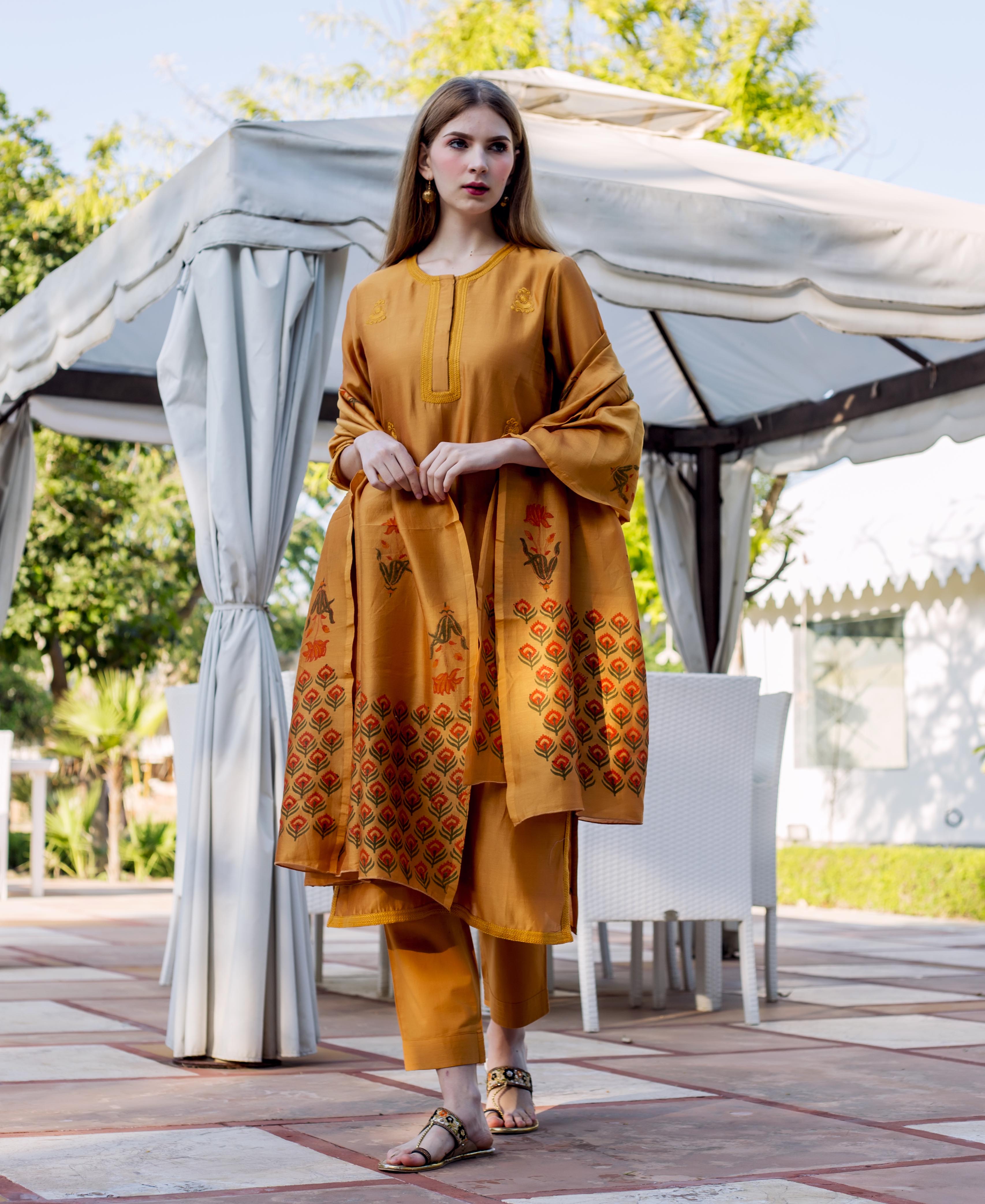 Model in autumn rust embroidered kurta set with matching pants and block-printed dupatta.