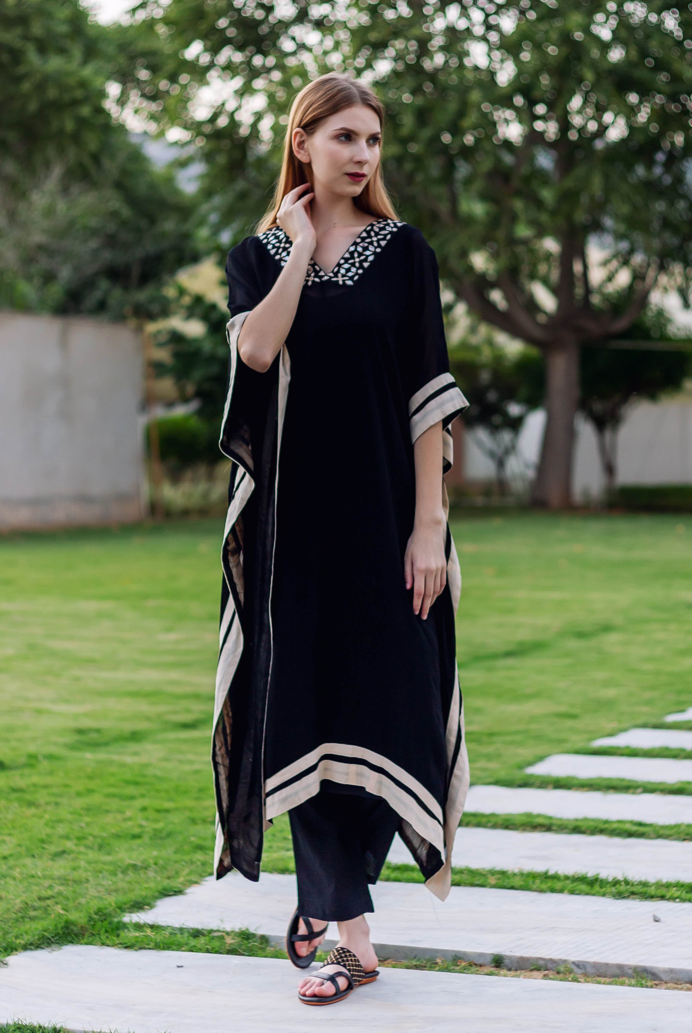Model in black kaftan featuring white embroidered V-neck, cream trim, and black pants.