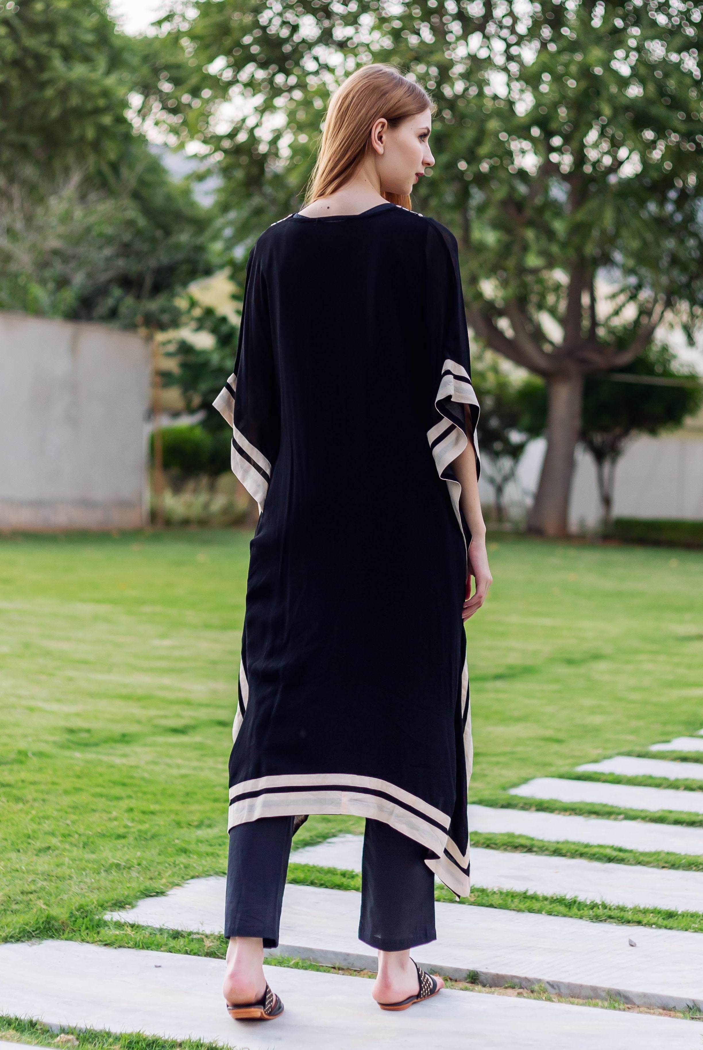 Model's back in black kaftan featuring beige striped sleeves and bottom hem.