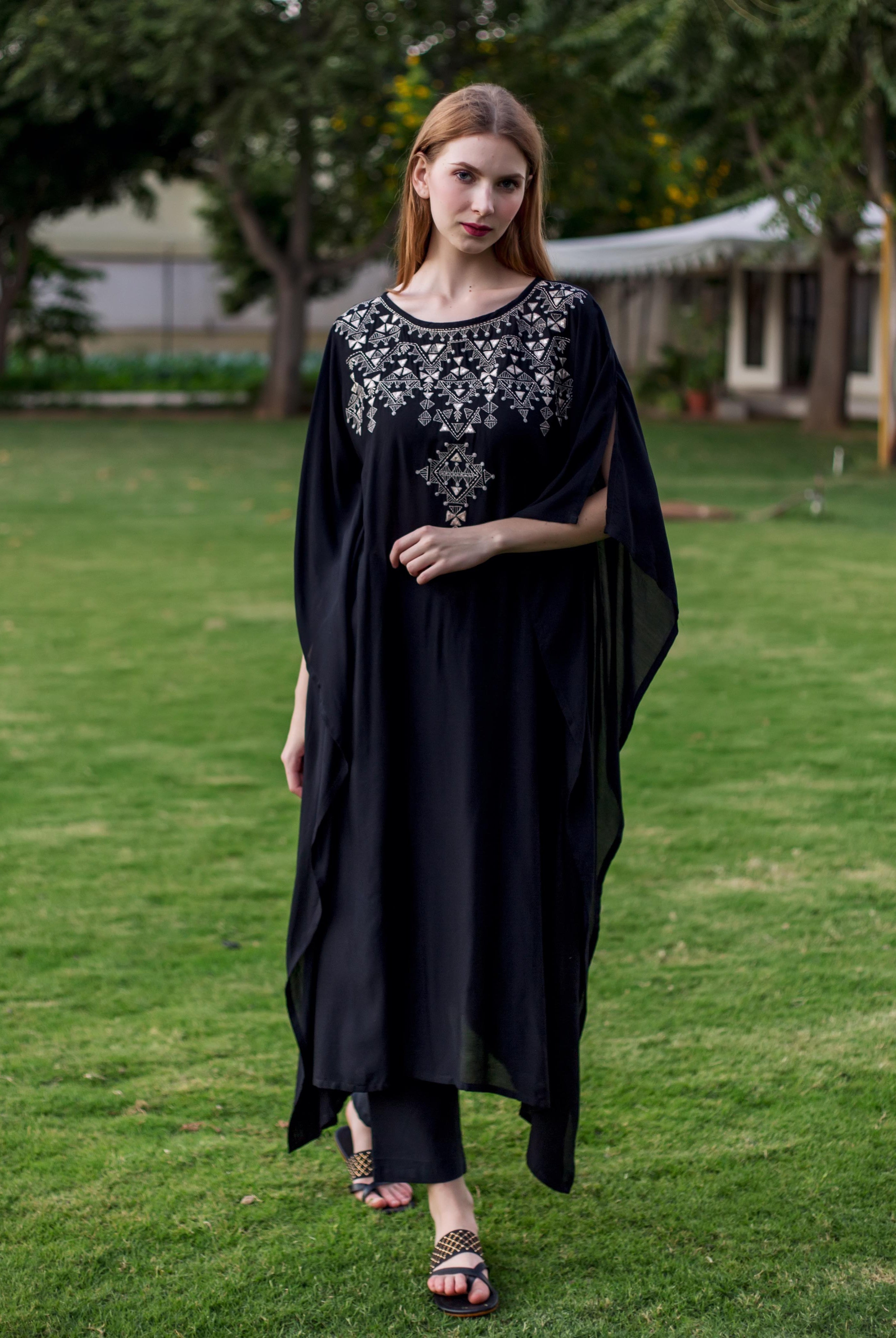 Front view of a model wearing a black muslin kaftan with silver geometric embroidery.