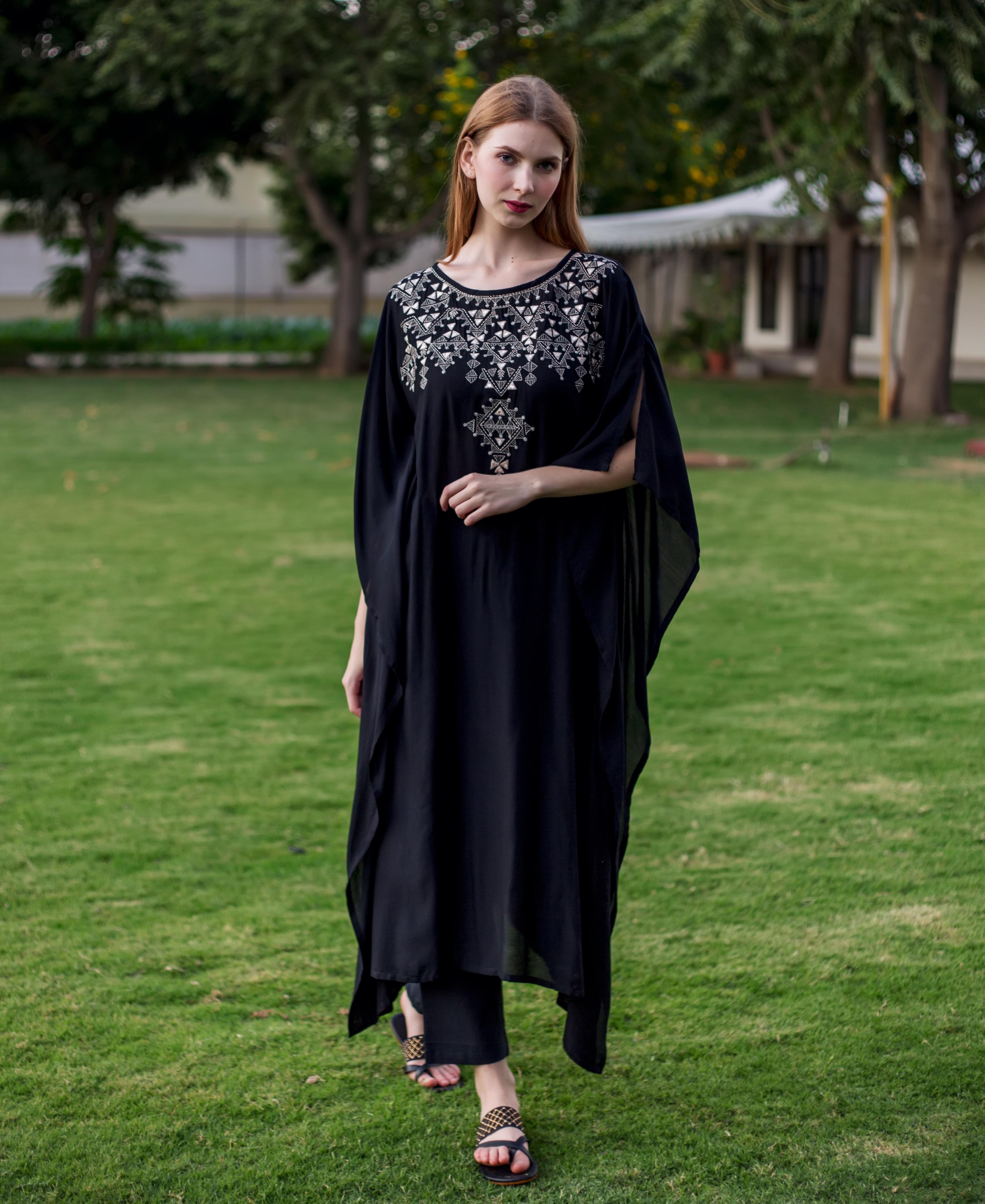 Front view of a model wearing a black muslin kaftan with silver geometric embroidery.