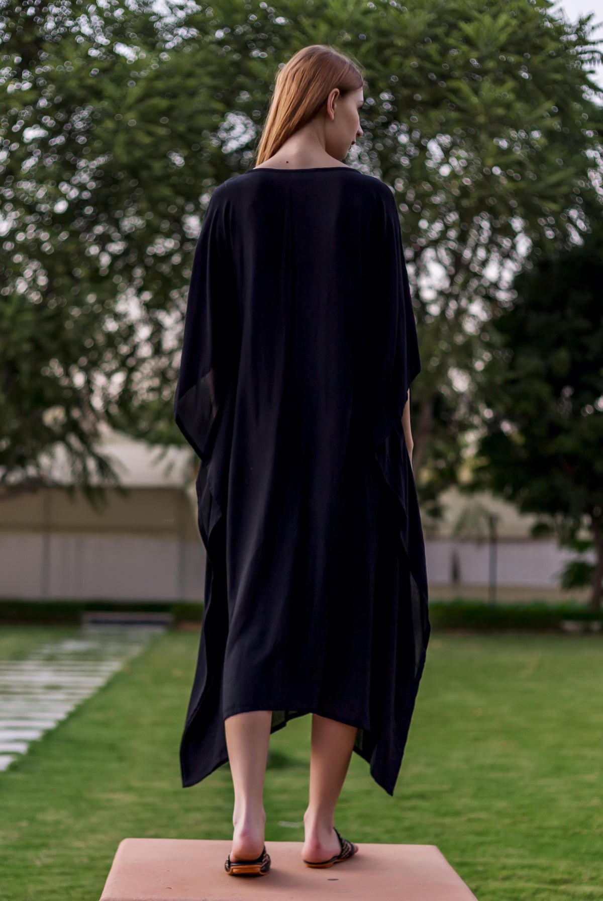 Full back view of a woman wearing a long, plain black muslin kaftan.