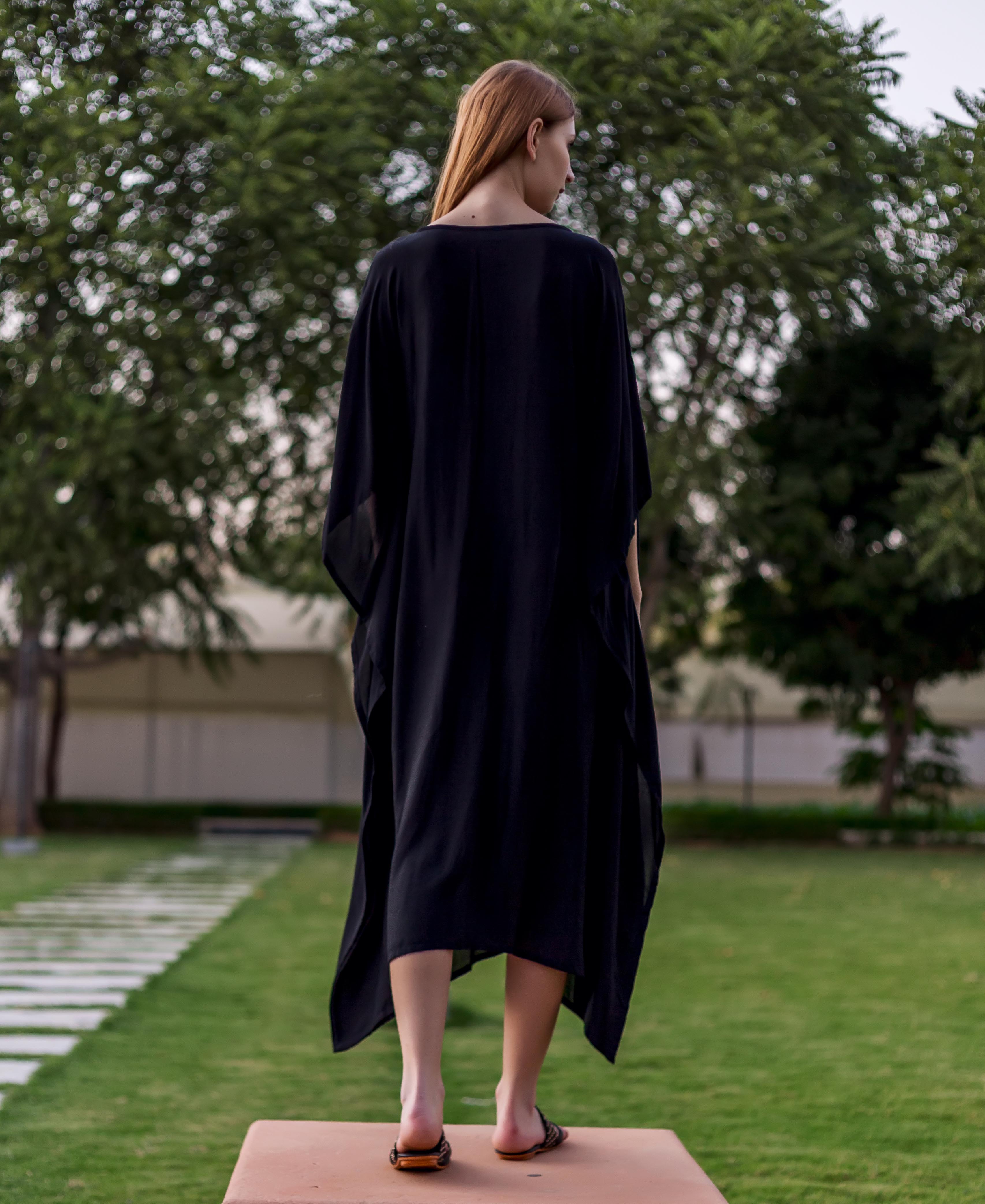 Full back view of a woman wearing a long, plain black muslin kaftan.