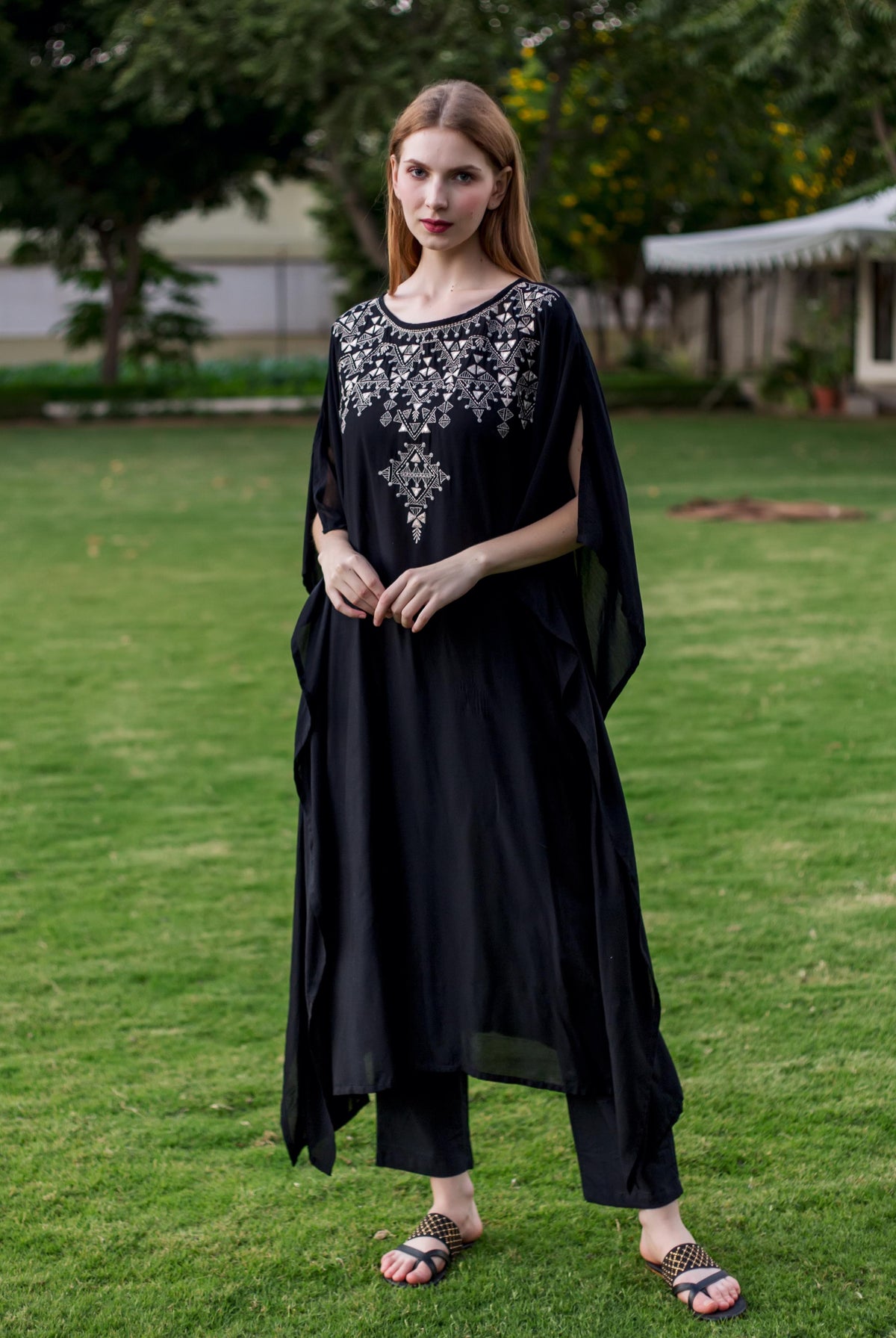 Front view of a model in a black muslin kaftan with intricate white geometric embroidery.
