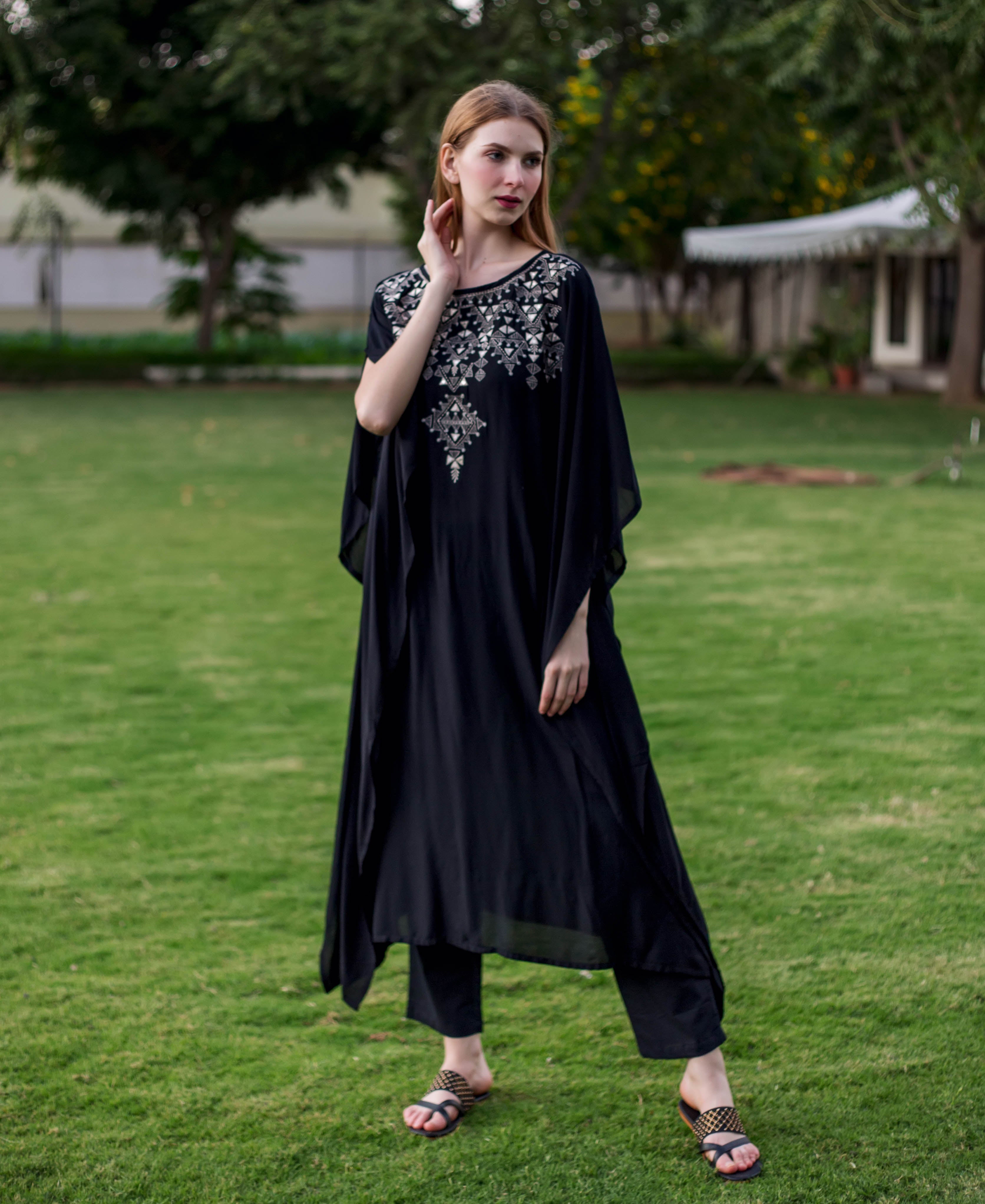 Full front view of model in black muslin kaftan with silver geometric embroidery and pants.