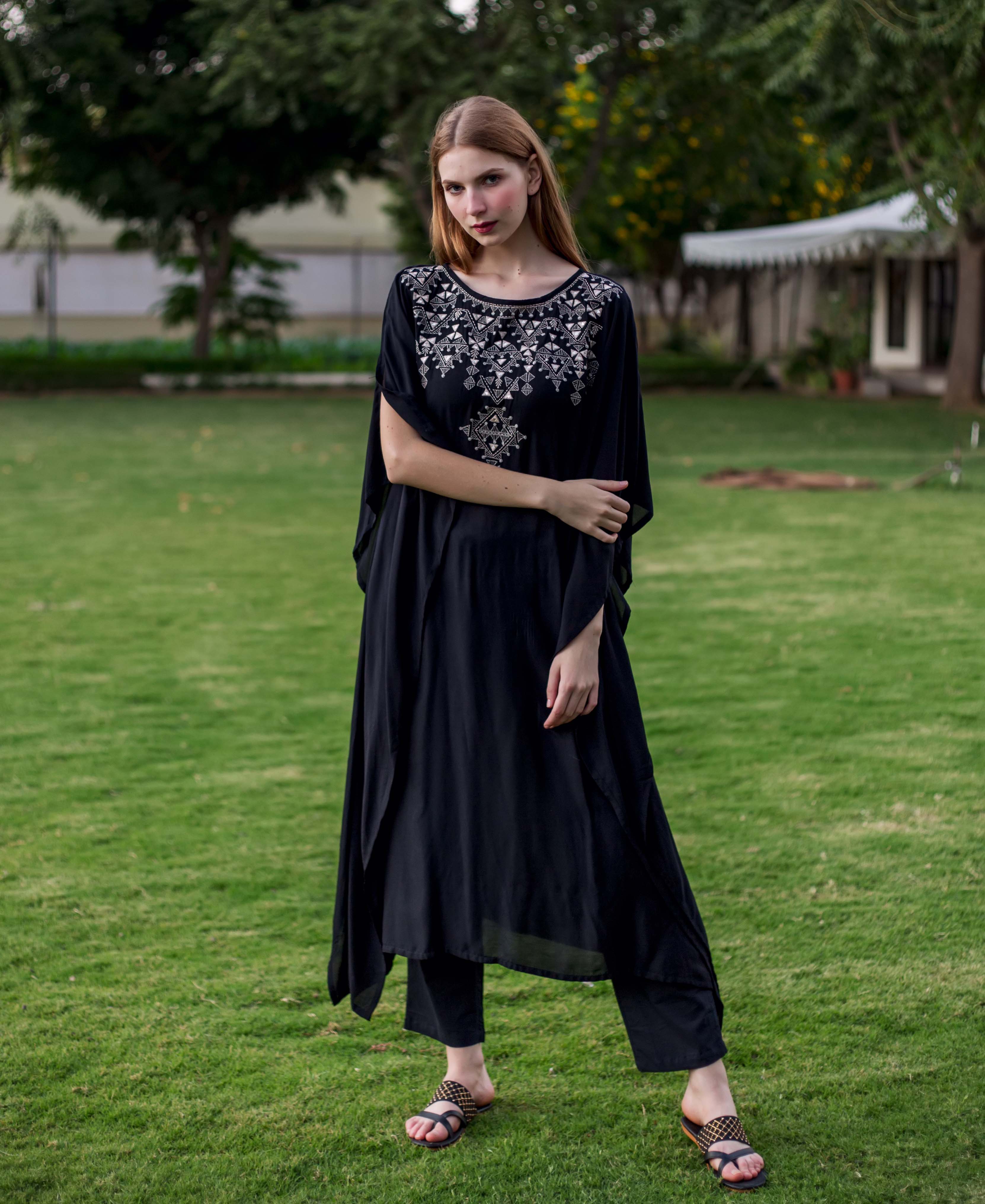 Model in black kaftan with intricate silver geometric embroidery and matching pants.