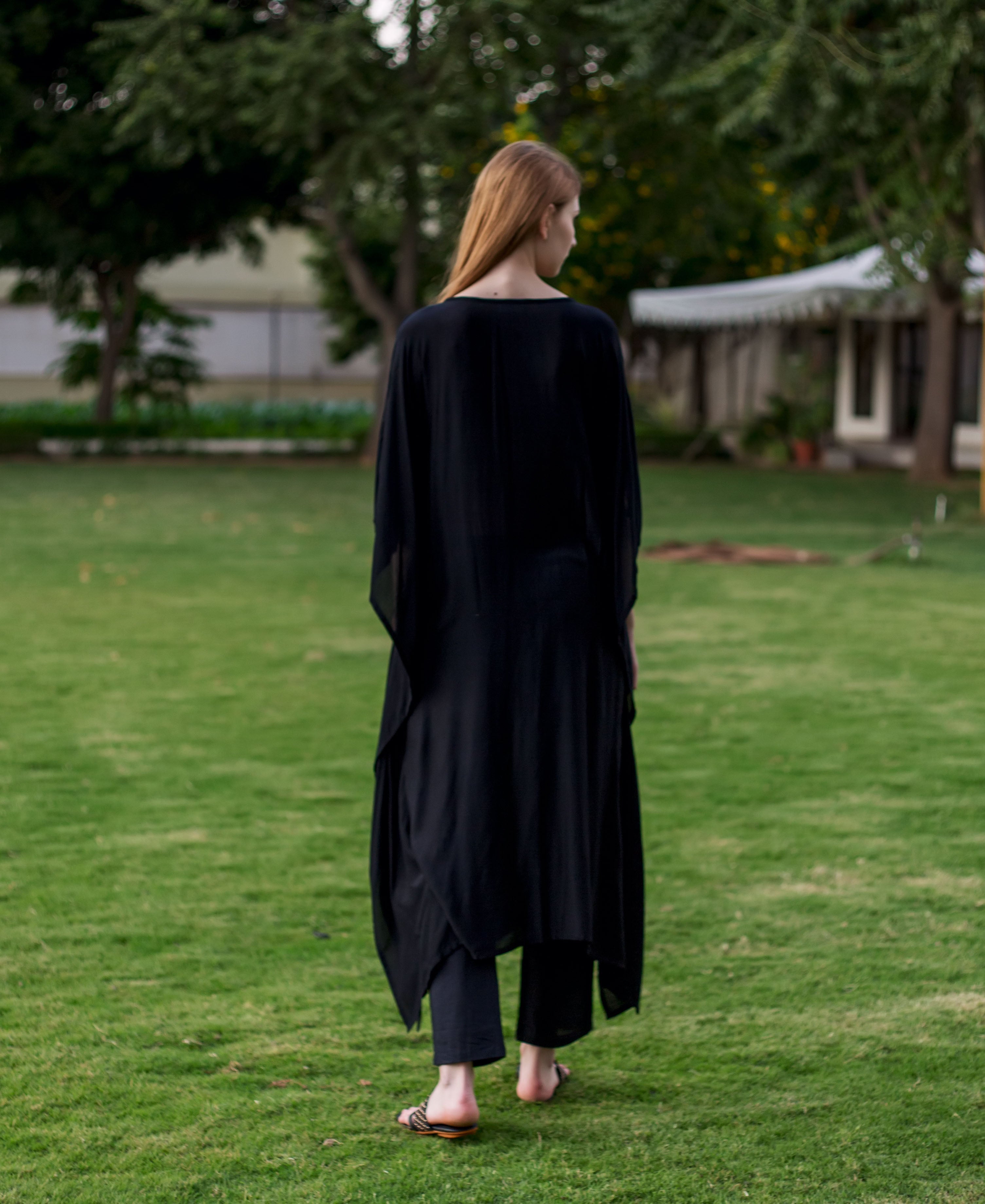A model wearing a black, long-sleeved kaftan with an embroidered design on the front.