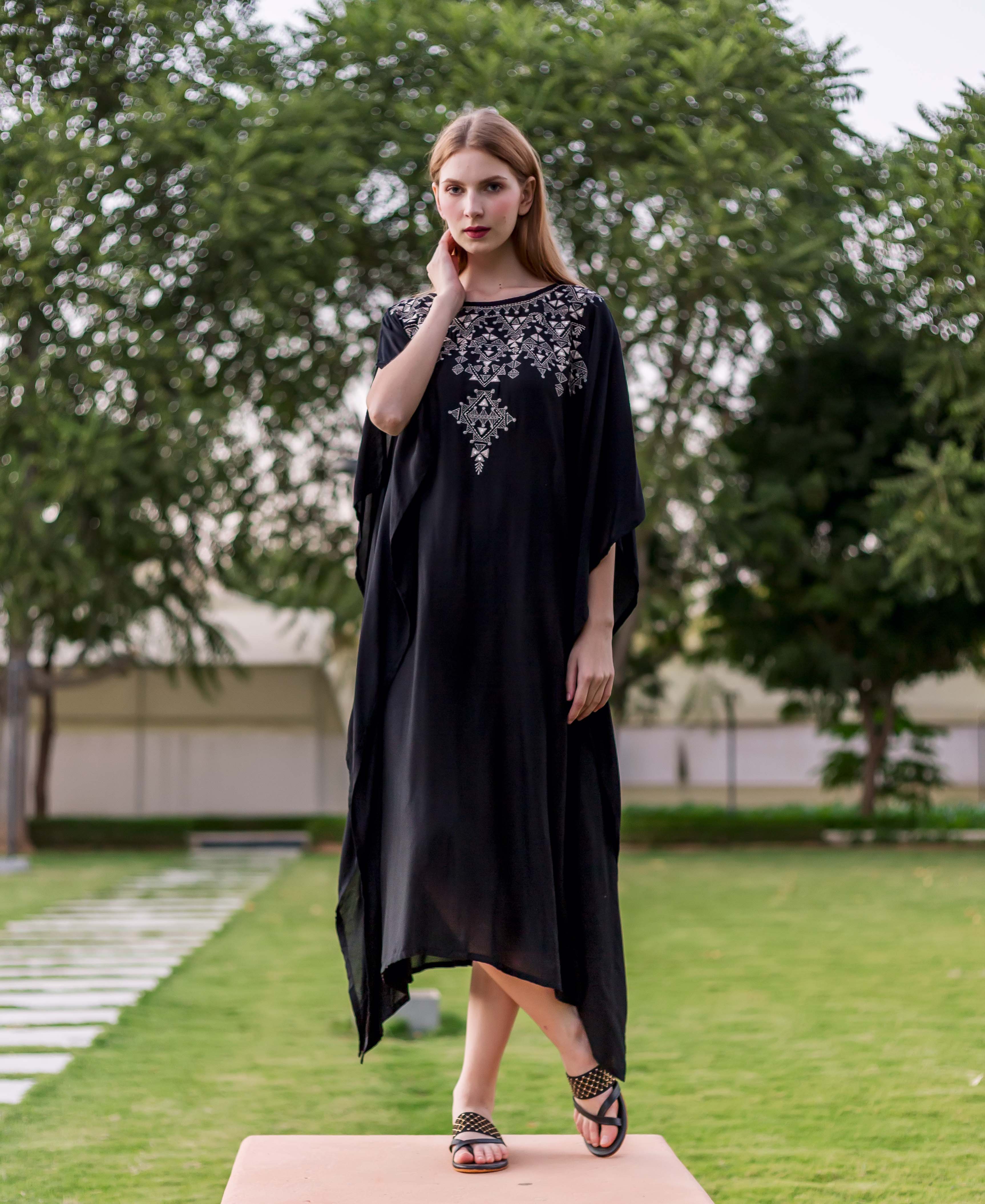 Full-length front view of model in black kaftan with intricate white ethnic embroidery.