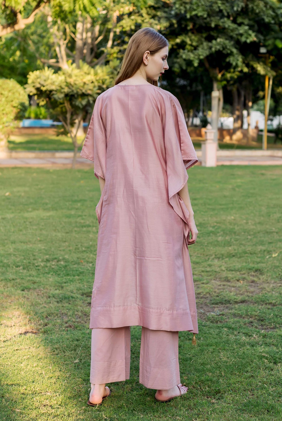 Model from behind, wearing a loose dusty pink hand-embroidered kaftan and matching wide-leg pants.
