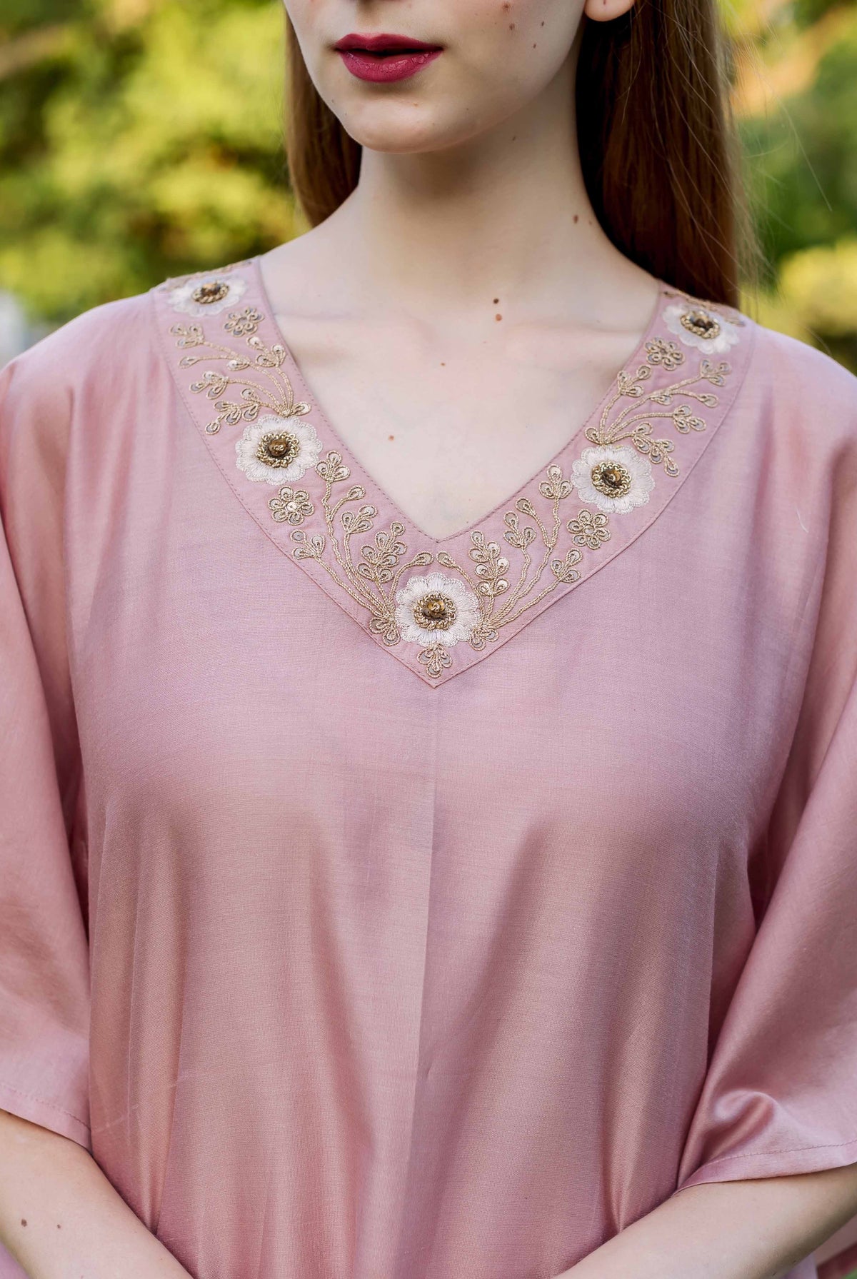 Dusty pink kaftan on model, showcasing intricate gold and white floral hand embroidery on V-neck.