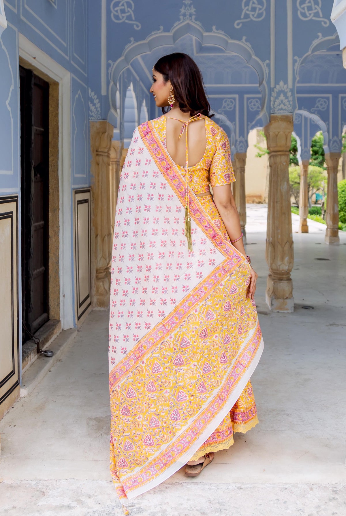 Back view of model in yellow, pink, and white hand block printed lehenga set with dupatta.