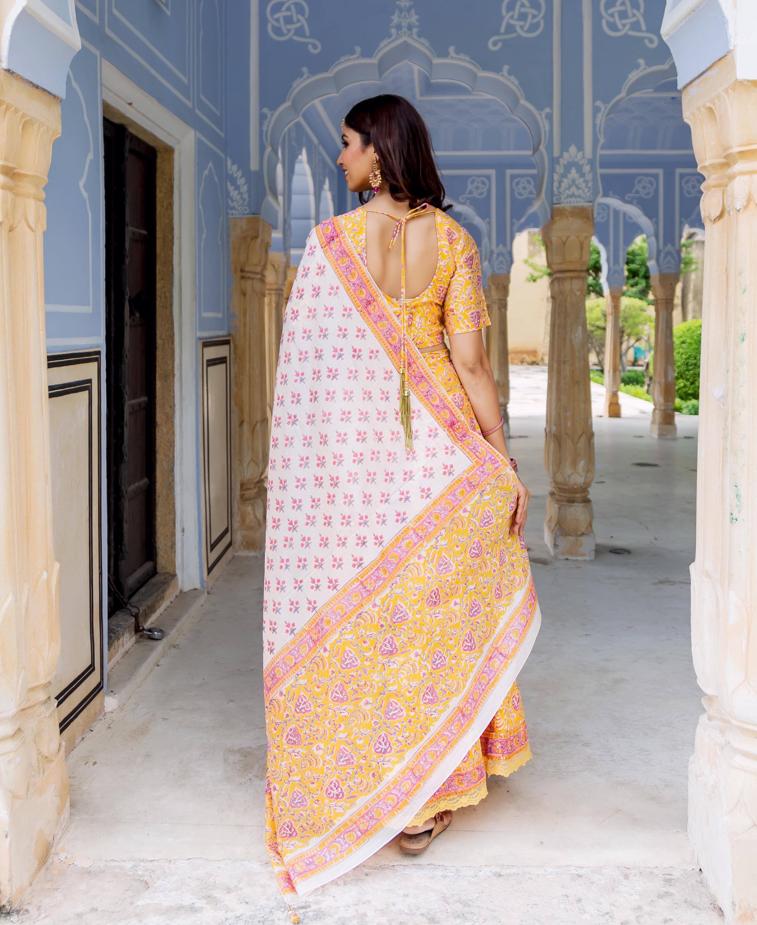 Back view of model in yellow, pink, and white hand block printed lehenga set with dupatta.