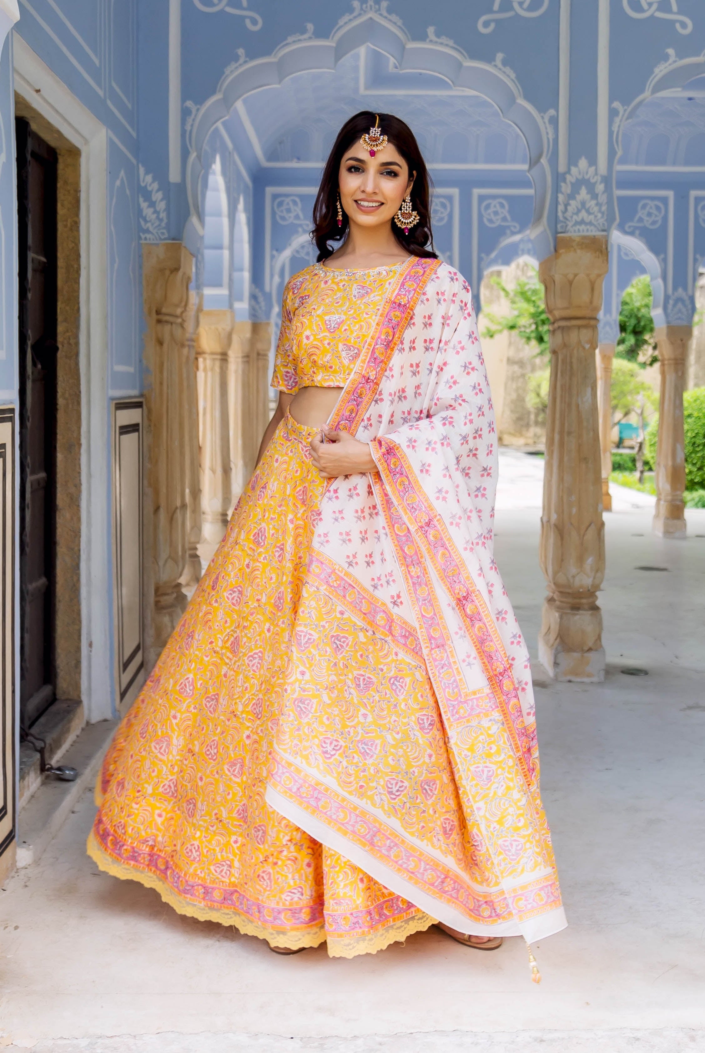 Smiling model in yellow and pink hand-block printed lehenga set with white dupatta.