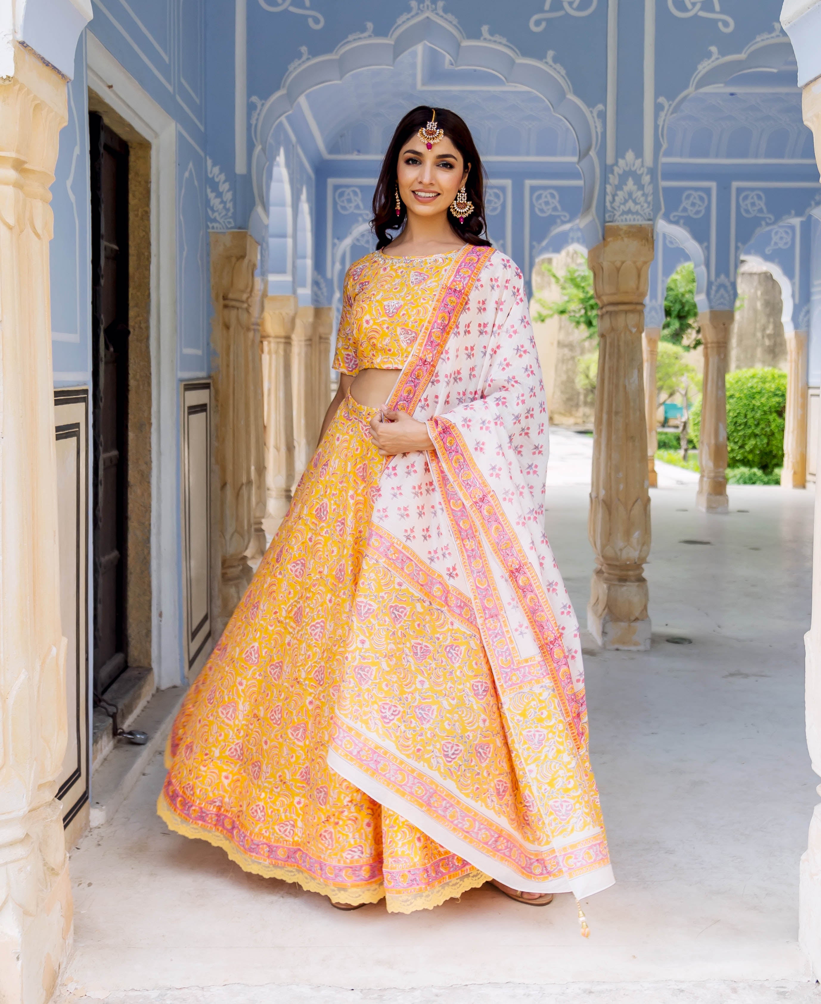 Smiling model in yellow and pink hand-block printed lehenga set with white dupatta.