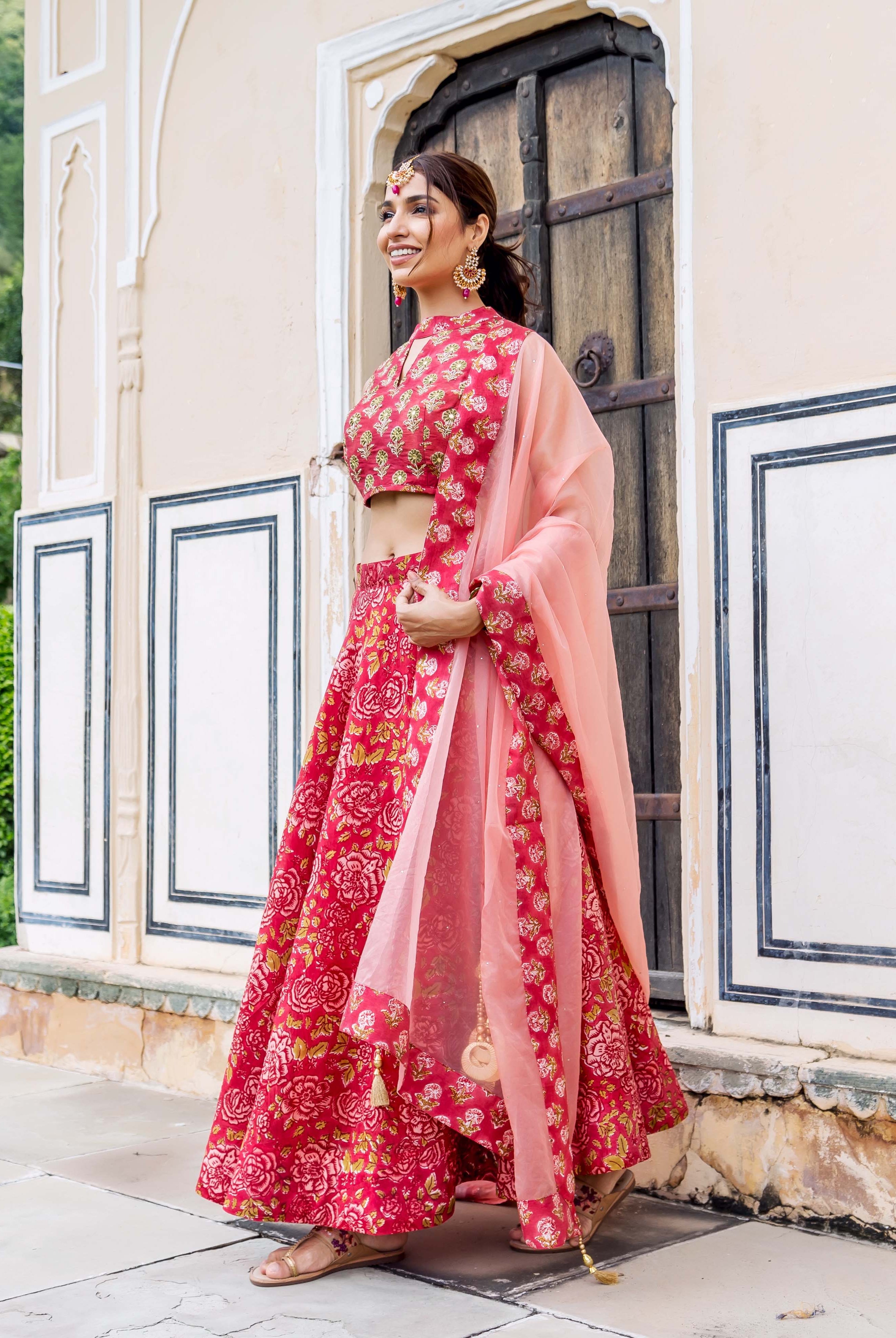 Smiling woman in a red hand block printed floral lehenga set with a peach dupatta.