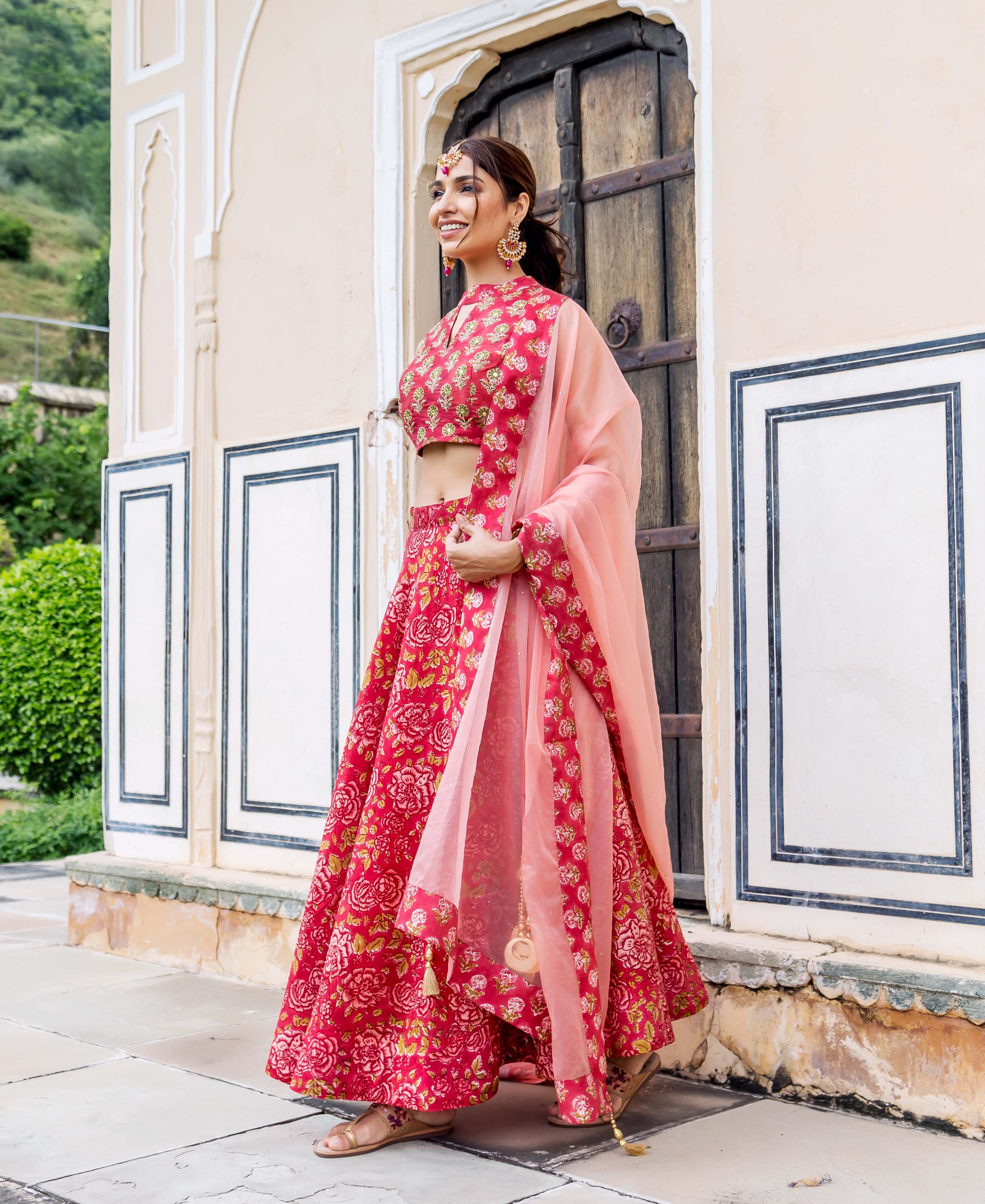 Smiling woman in a red hand block printed floral lehenga set with a peach dupatta.