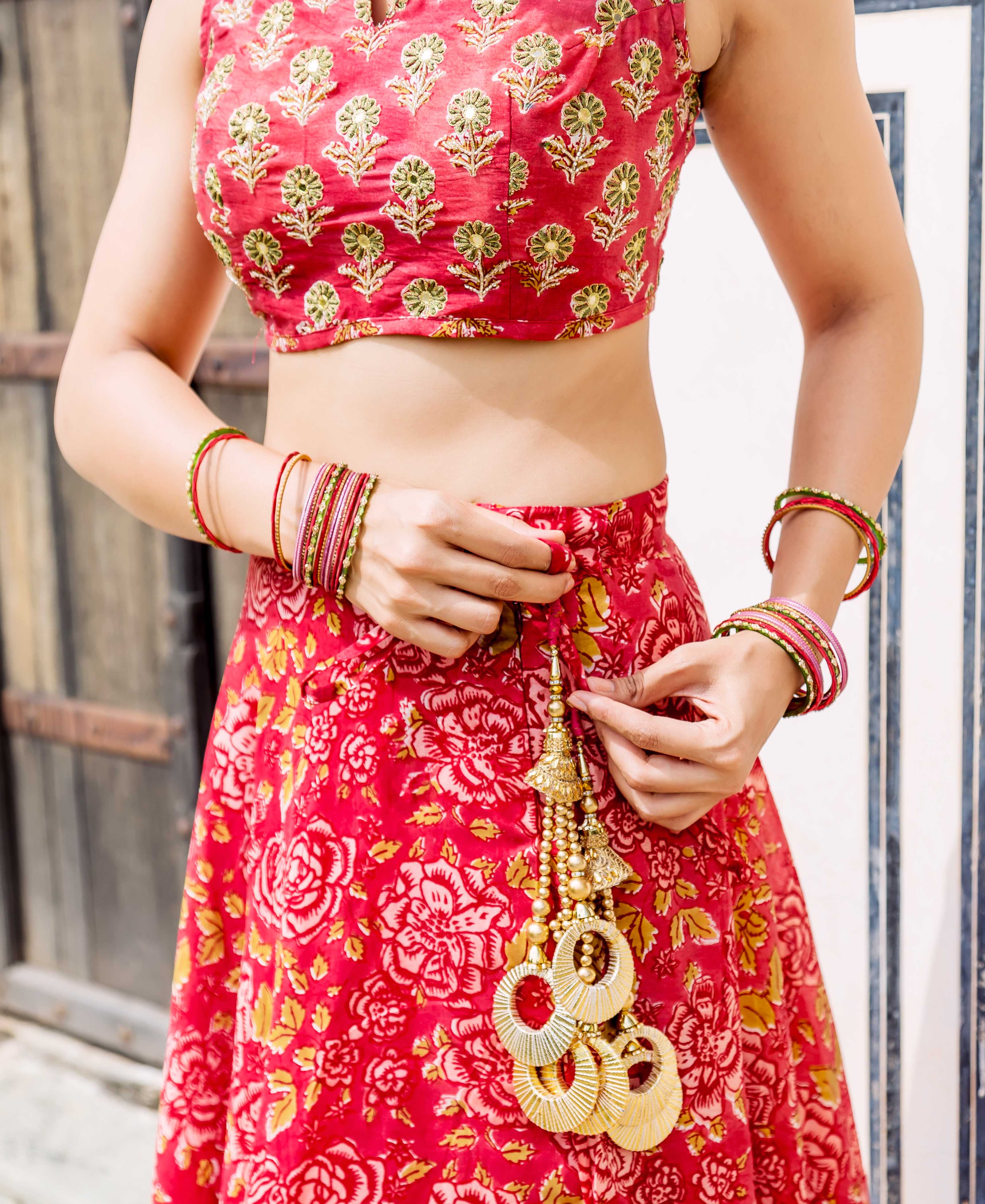 Red hand-block printed floral lehenga set with a gold embroidered blouse and ornate tassels.