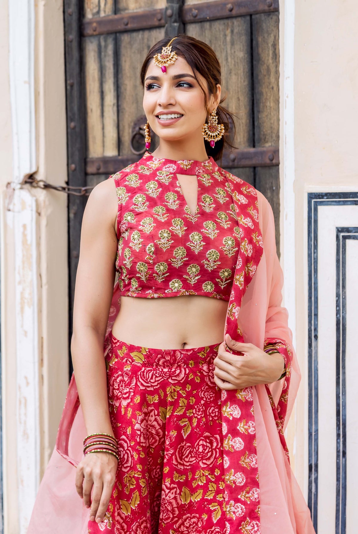 Smiling model in red hand-block printed lehenga set, embroidered top, and pink dupatta.