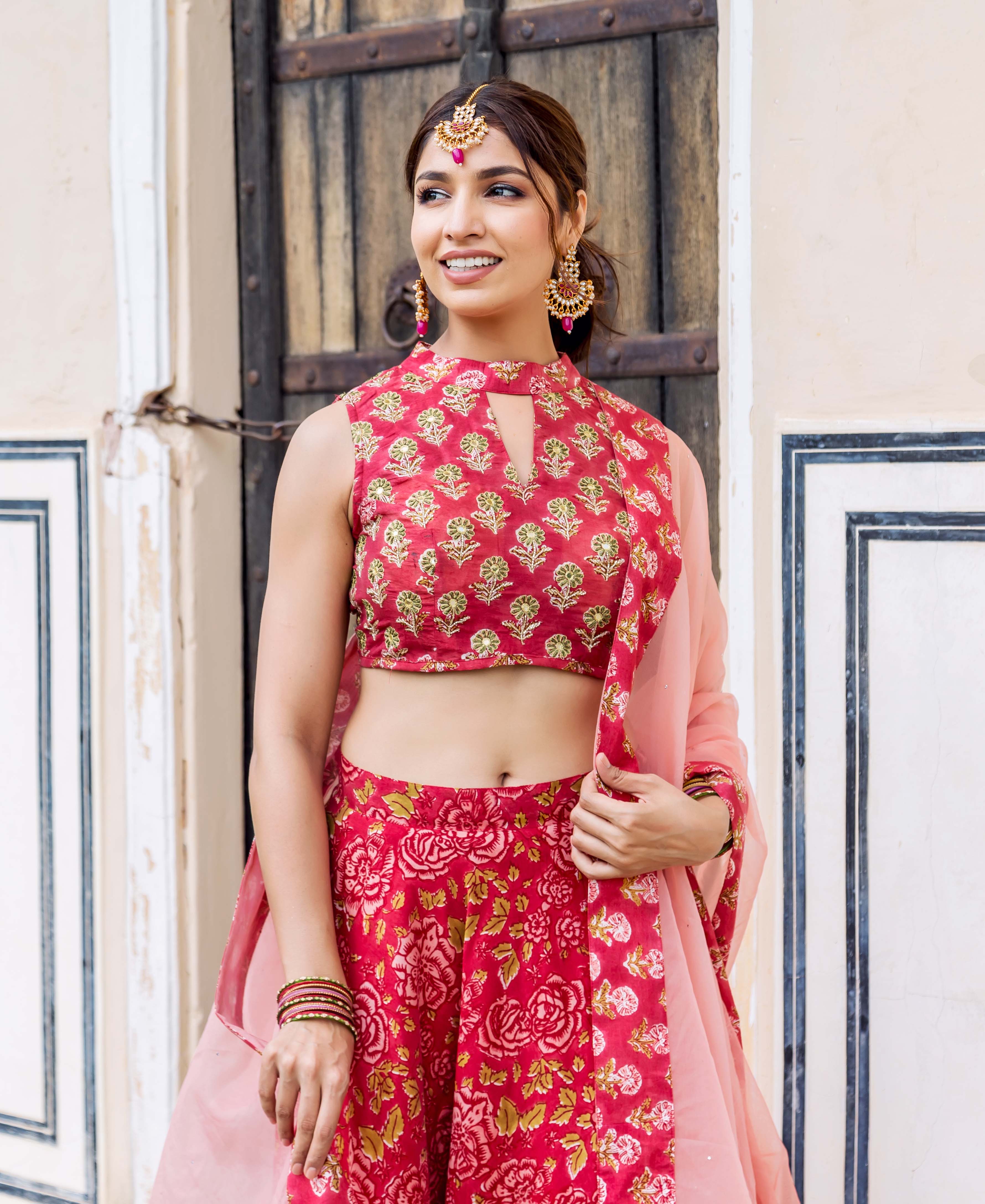 Smiling model in red hand-block printed lehenga set, embroidered top, and pink dupatta.