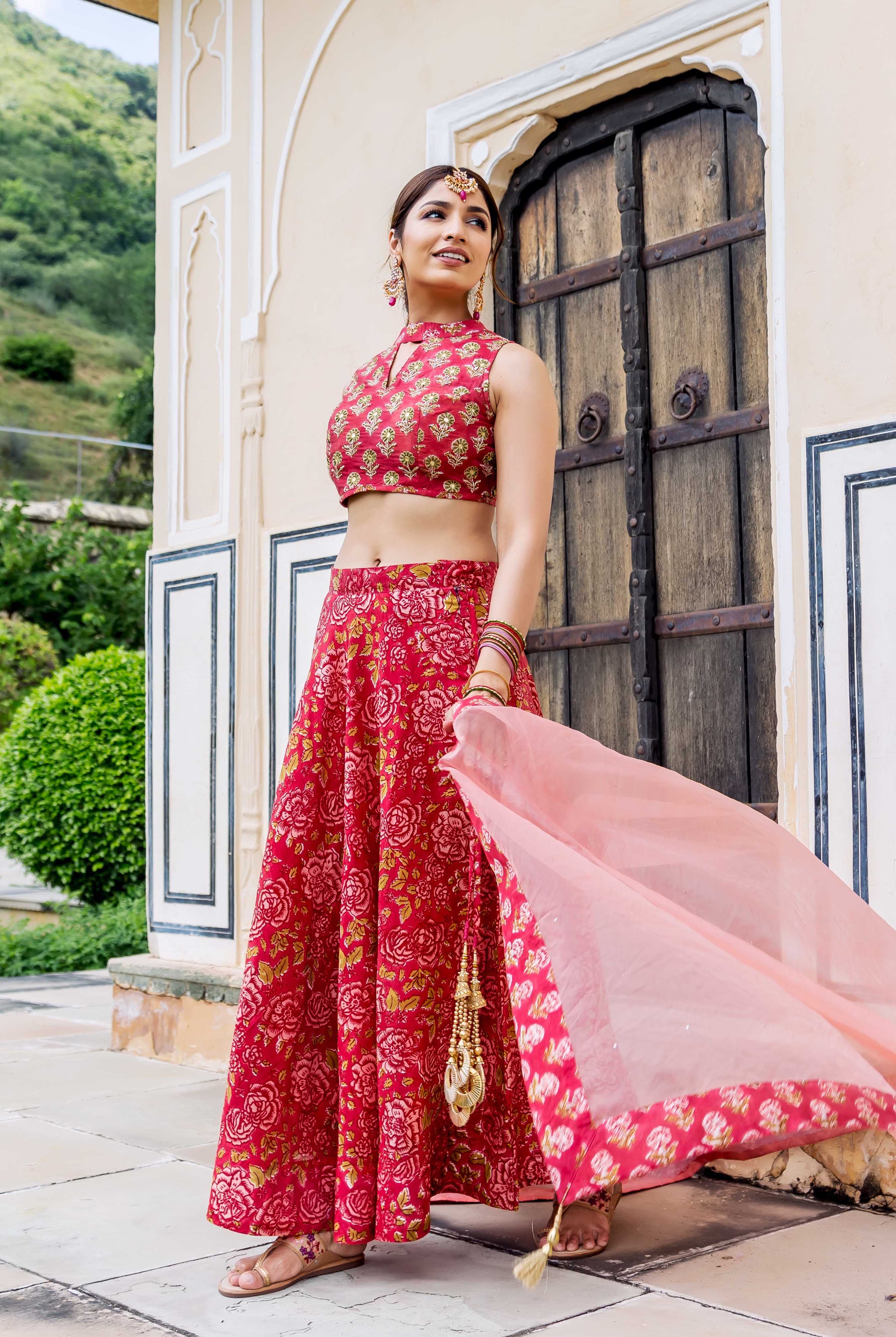Model in red hand-block printed floral lehenga and crop top with a sheer pink dupatta.