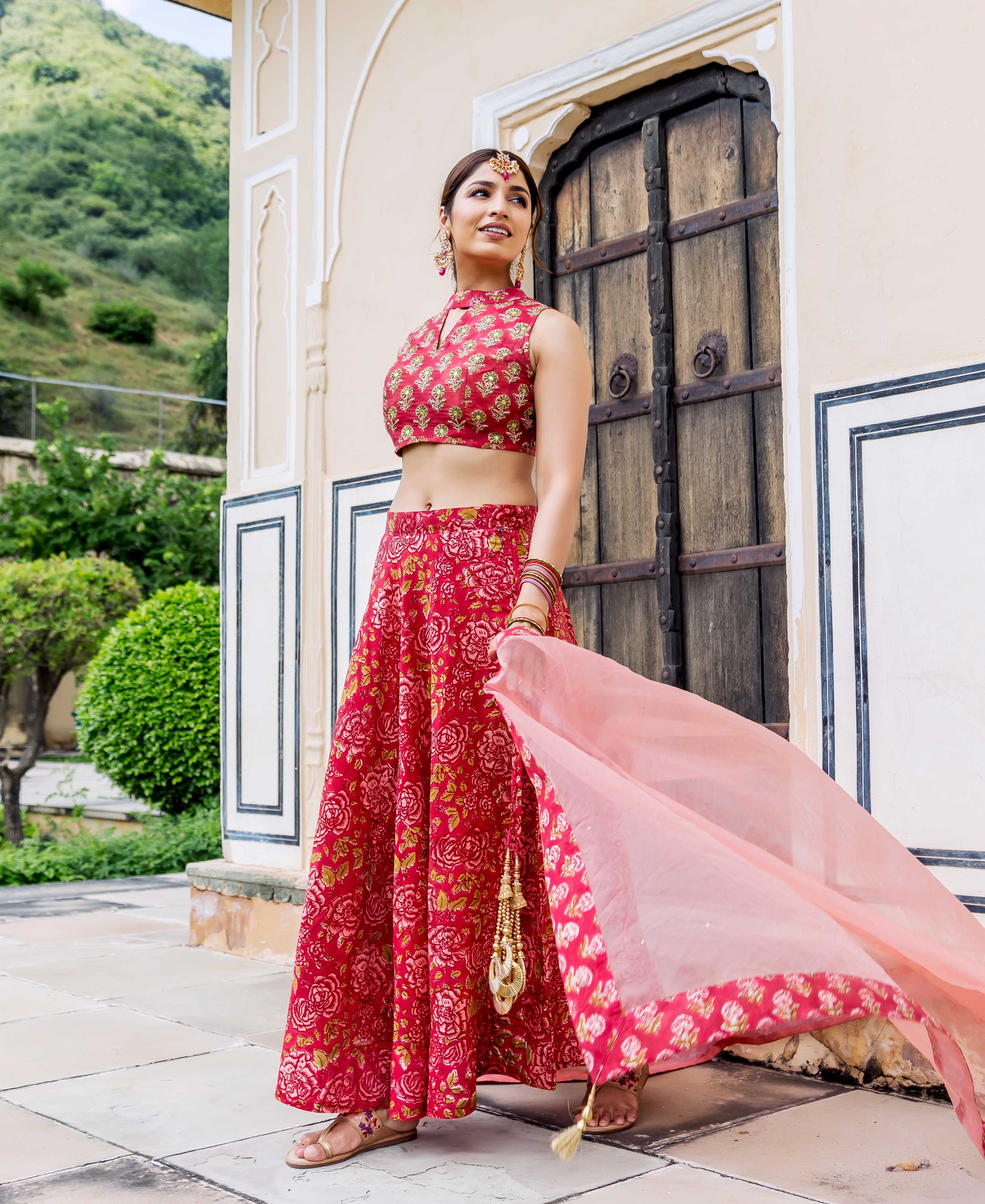 Model in red hand-block printed floral lehenga and crop top with a sheer pink dupatta.