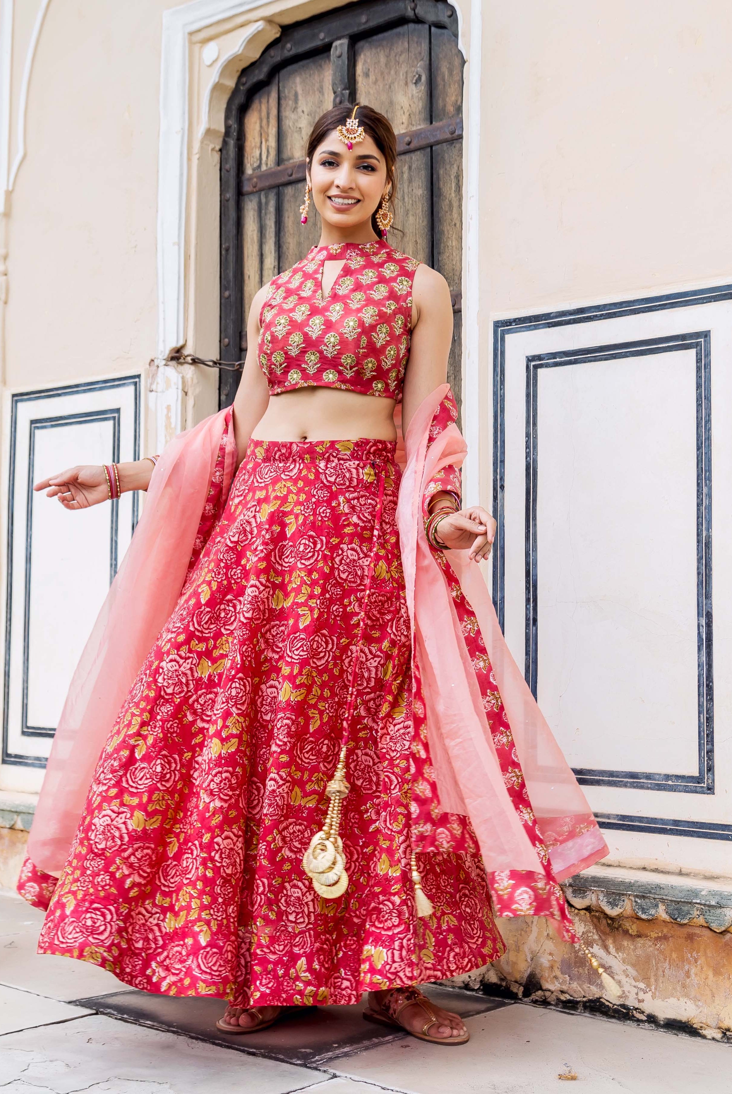 Smiling model wearing a vibrant pink floral hand-block printed lehenga set with a sheer dupatta.