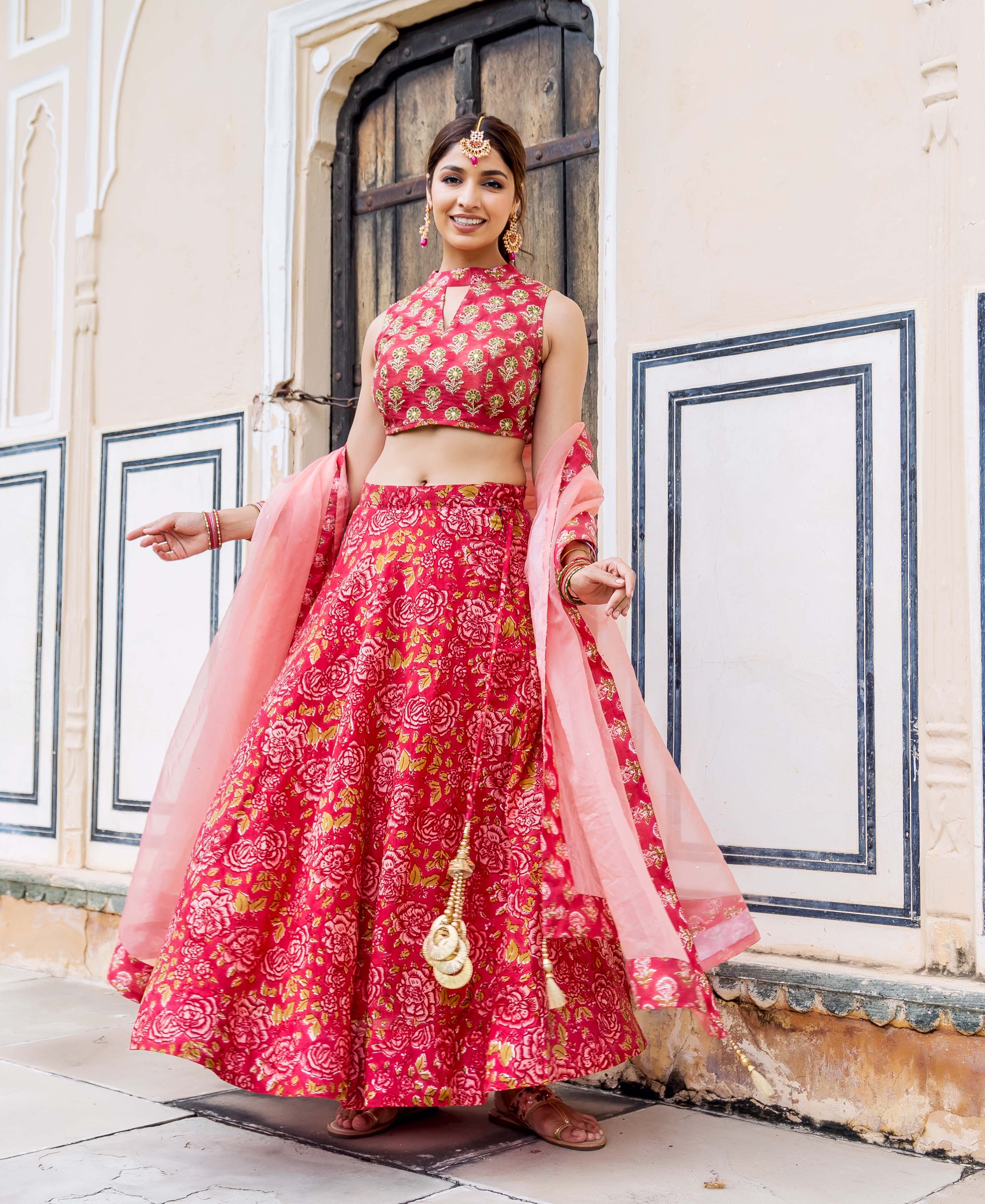 Smiling model wearing a vibrant pink floral hand-block printed lehenga set with a sheer dupatta.
