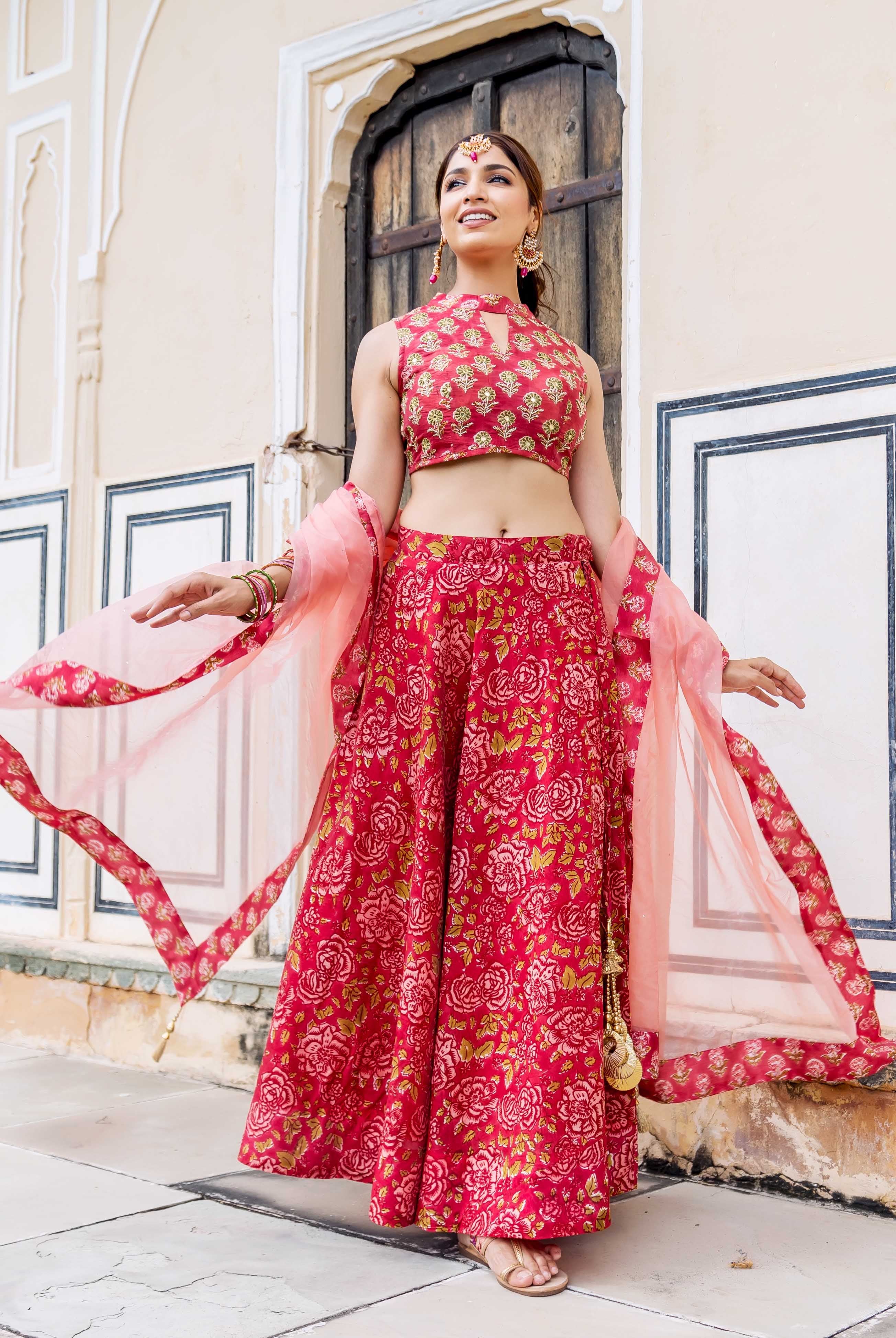 Smiling model in red hand block printed floral lehenga set with flowing dupatta.