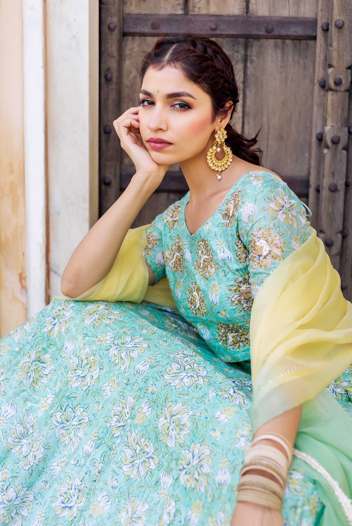 Model seated, wearing a mint green hand-block printed floral lehenga set with yellow dupatta.
