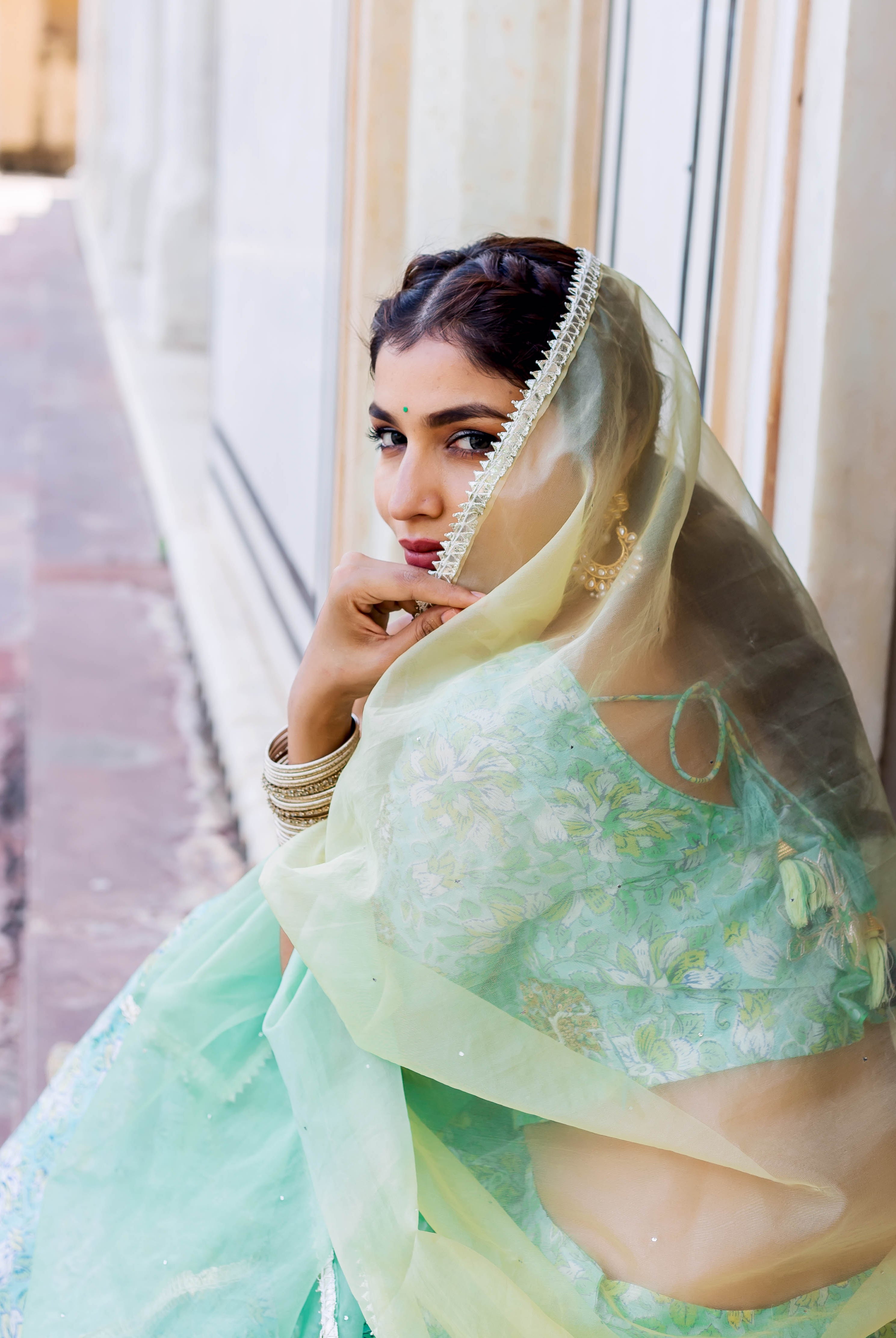 Seated woman in mint green hand-block-printed lehenga set with subtle embroidery and yellow dupatta.