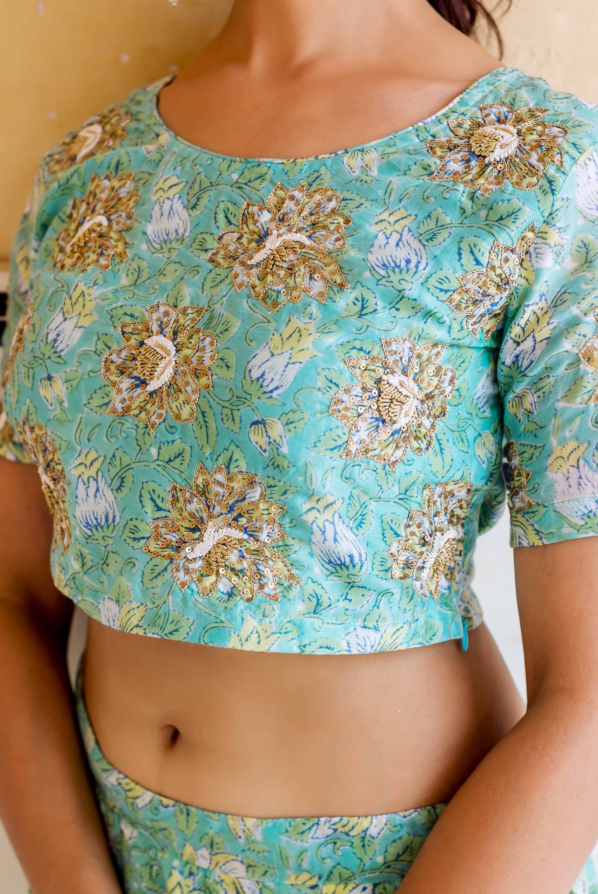 Model's torso in aqua hand-block printed crop top with gold floral embroidery.
