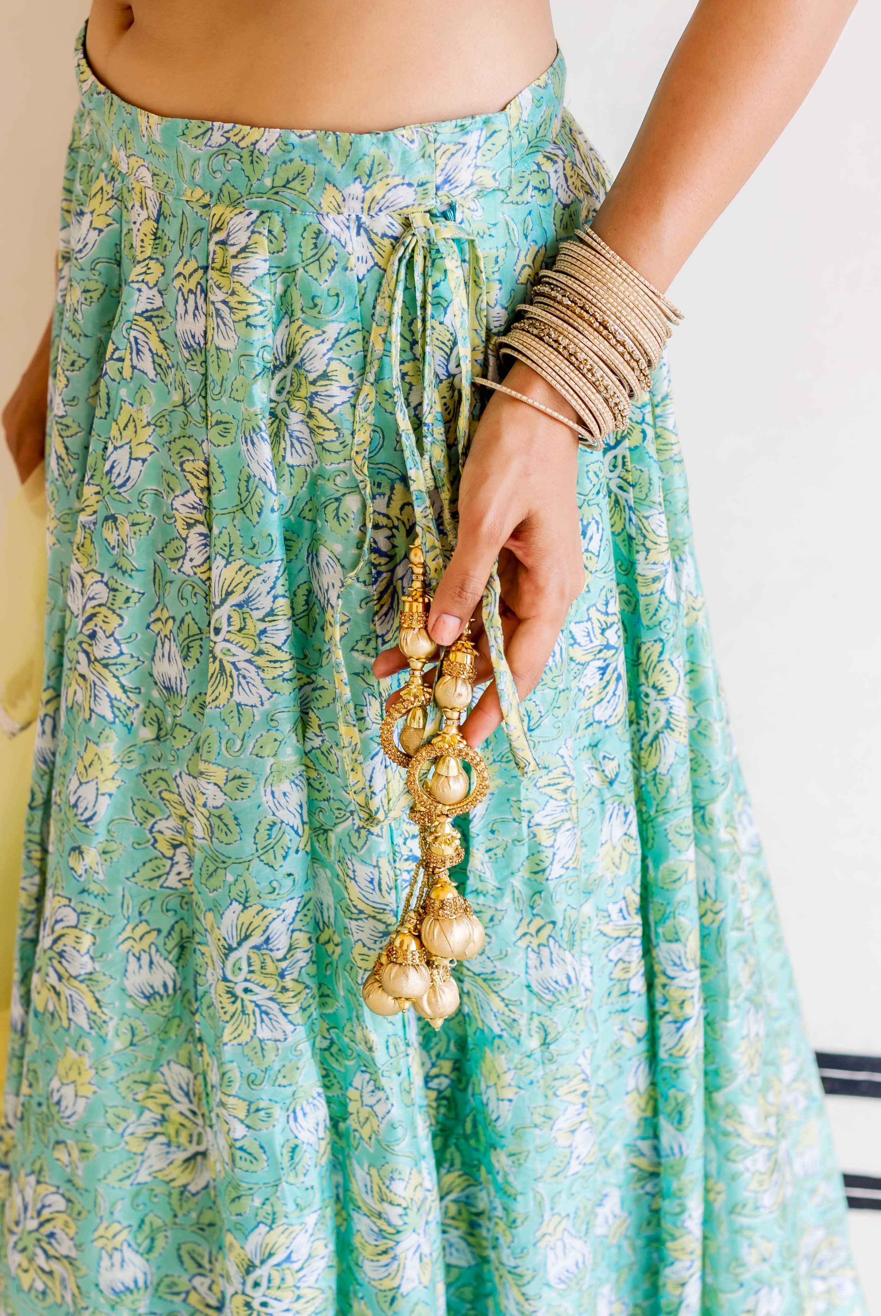 Close-up of a model wearing light green floral block print lehenga with golden tassels.